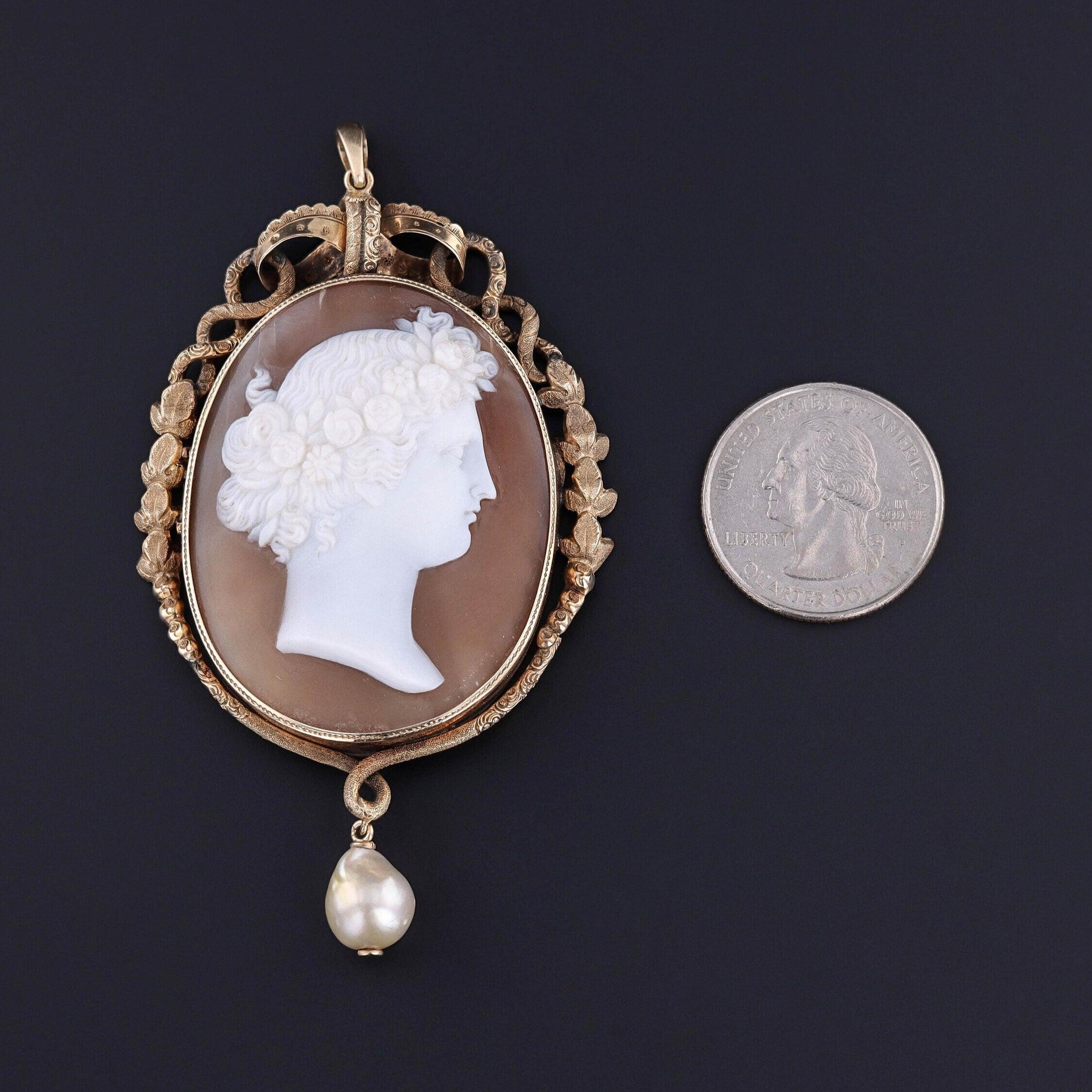 Ce pendentif ancien (vers 1870) présente un camée en coquillage sculpté d'une belle femme, serti dans de l'or 12k avec une perle d'eau douce en pendentif.

La pièce mesure 3,3 pouces du haut de la bague au bas par 1,9 pouces de large, et elle est en