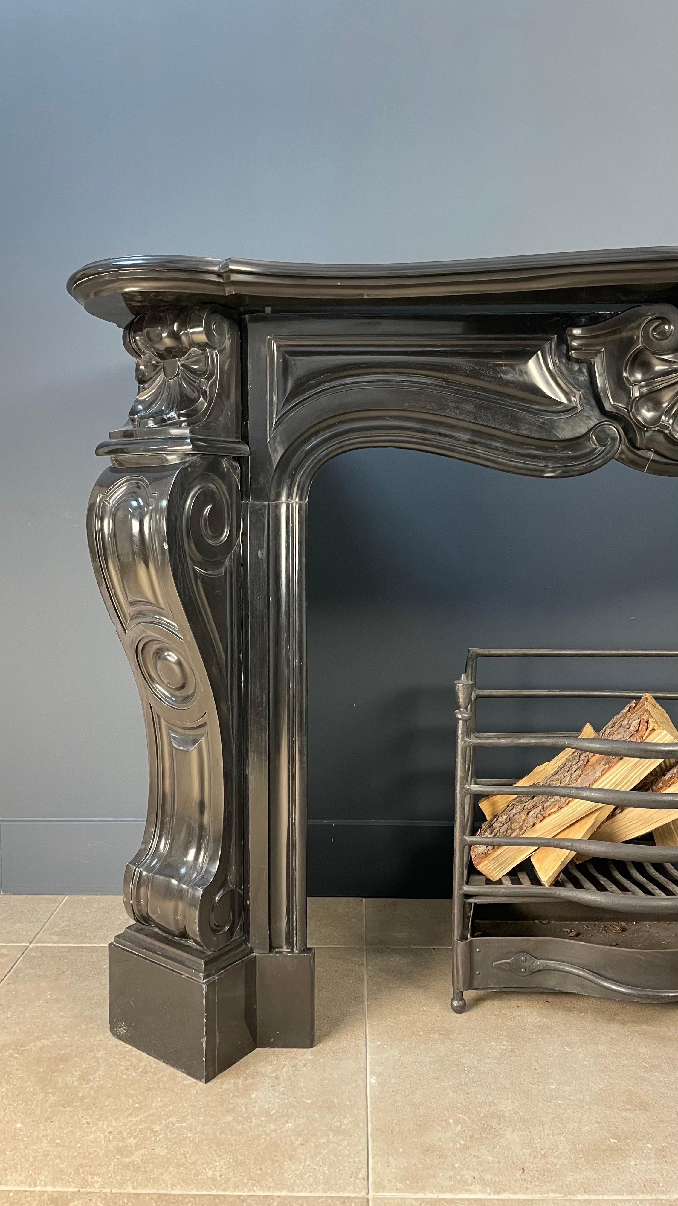 A luxurious black marble antique fireplace in black gold Noir de Mazy marble. This circular fireplace has a luxurious look because the consoles are at an angle. In addition to the well-known shell, the front also features elegant millwork that