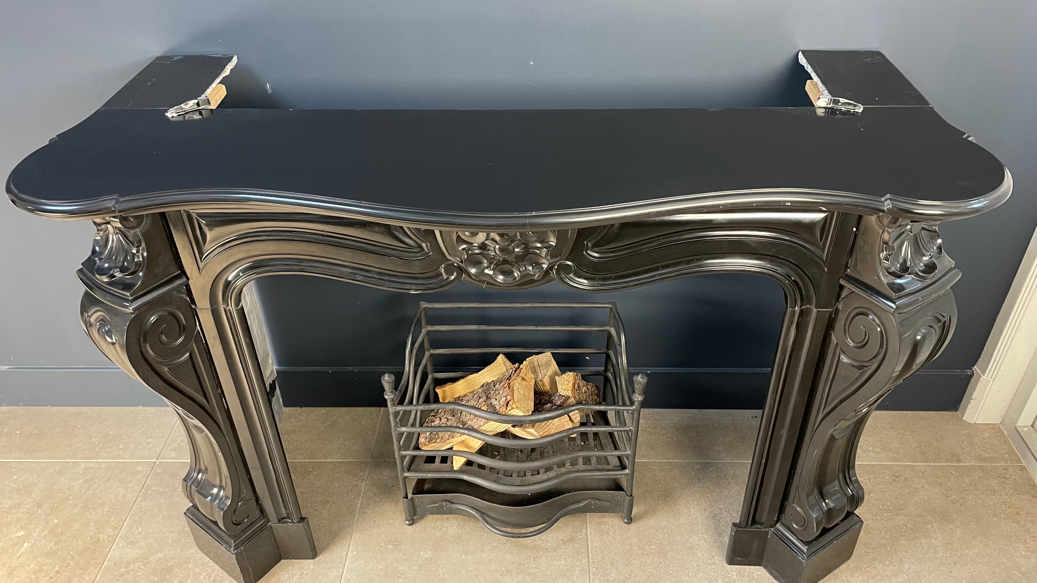 Introducing a sumptuous antique fireplace crafted from exquisite black gold Noir de Mazy marble. This opulent circular masterpiece exudes luxury with its uniquely angled consoles, elevating its aesthetic allure. Beyond the classic shell design, the