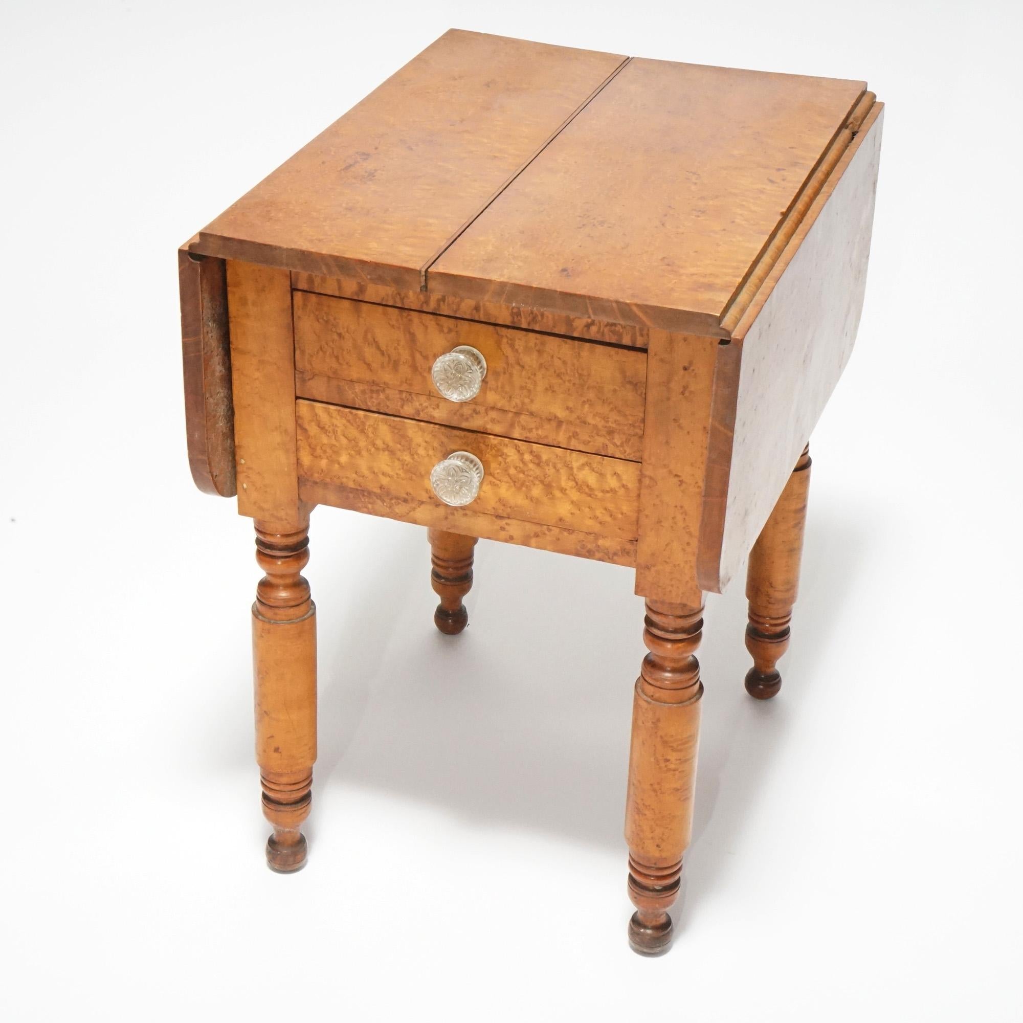 An antique Sheraton side stand offers birds eye maple construction with drop leaf top over double drawer case, raised on turned legs, c1840.

Measures- 28.75''H x 19.75''W x 24''D.