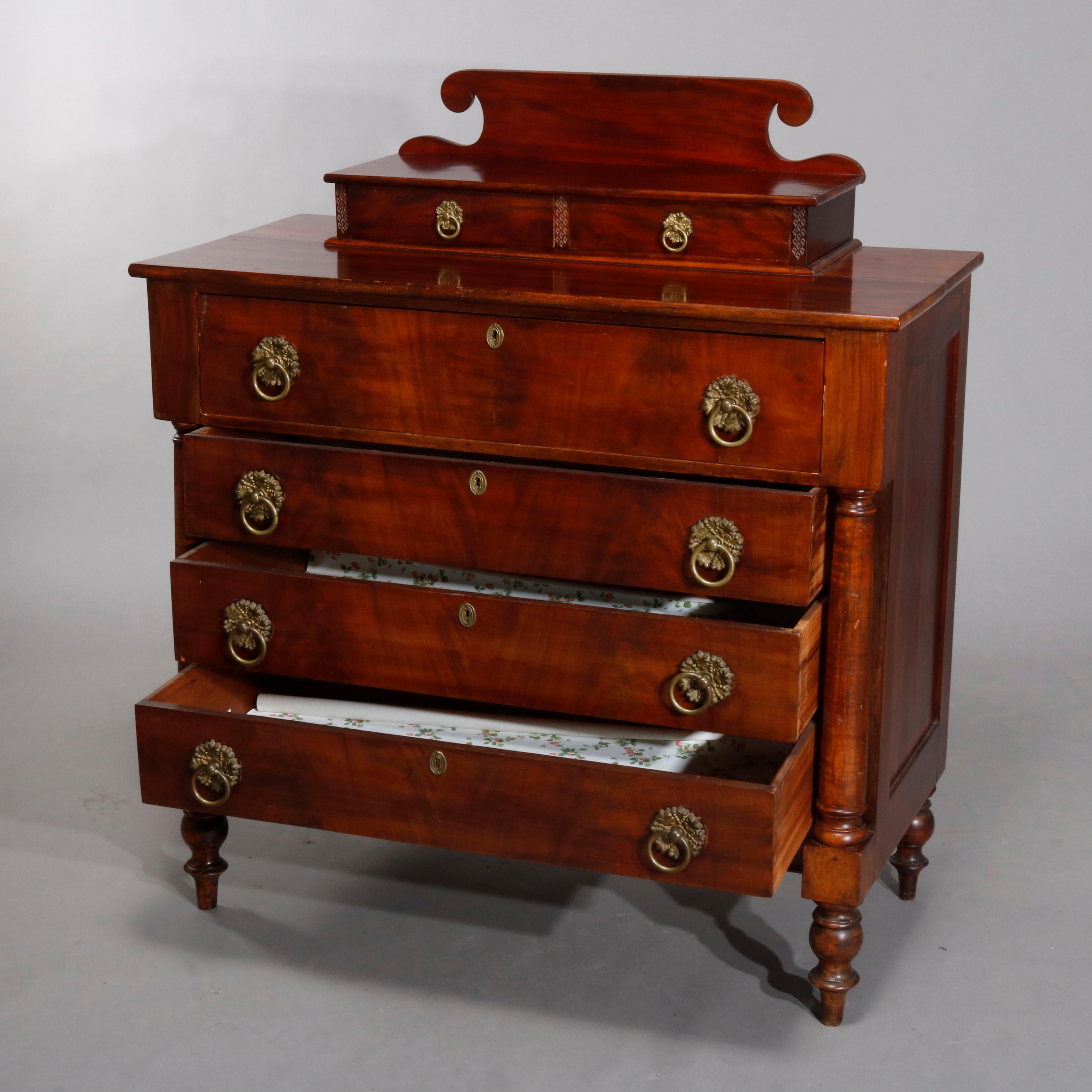 An antique Sheraton chest of drawers offers mahogany construction with scrolled backsplash and two glove boxes surmounting paneled case with large frieze drawer over three long drawers flanked with turned full columns, seated on turned turnip feet,