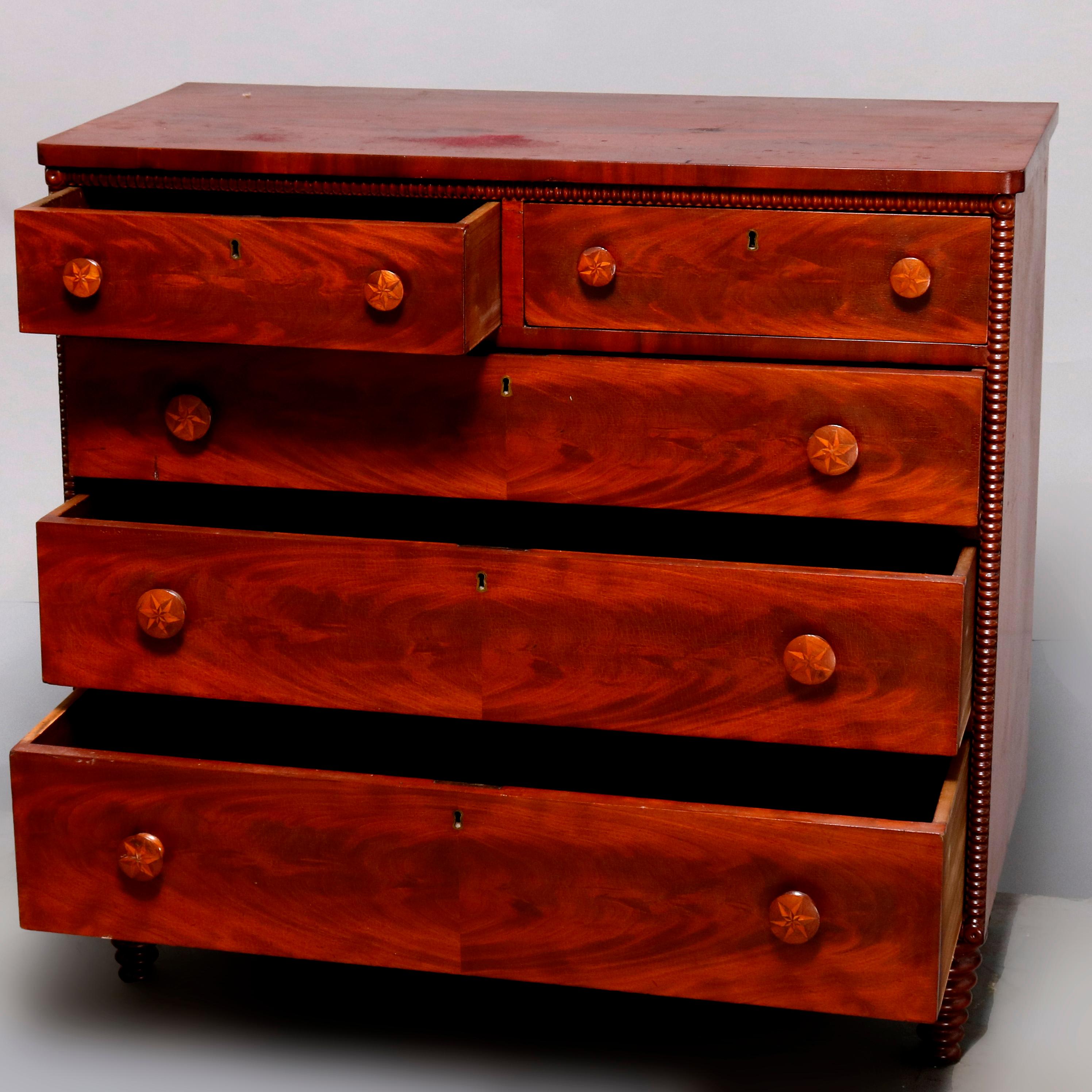 An antique Sheraton flame mahogany Folk Art chest of drawers offers case with spool carved border surrounding two small upper drawers over three long drawers, all with bookmatched facing and satinwood parquetry inlaid pulls having star design,