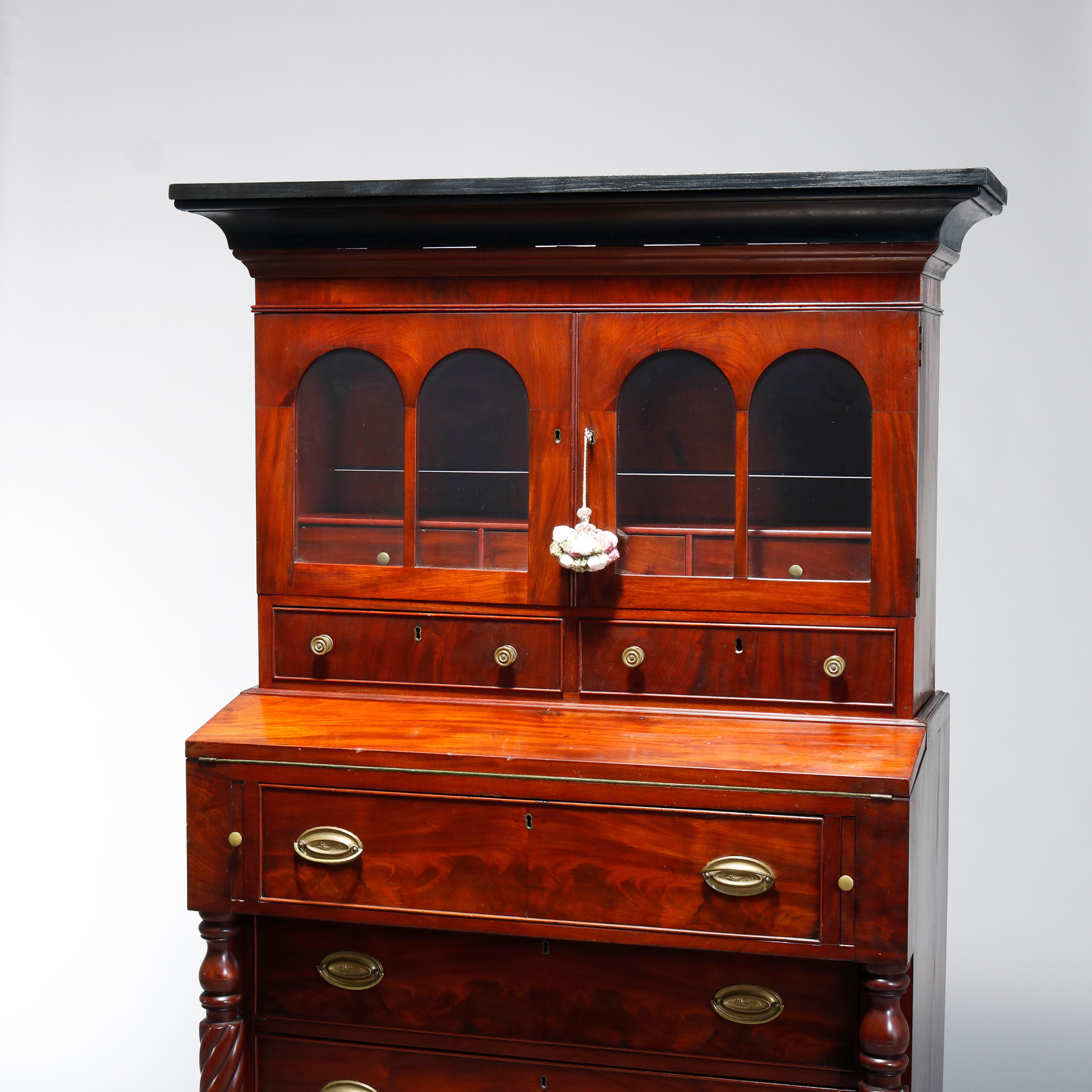 An antique Sheraton secretary offers flame mahogany construction and upper step-back bookcase with double doors having arched windows opening to shelved interior with lower drawers over lower case having drop down desk surmounting two long drawers