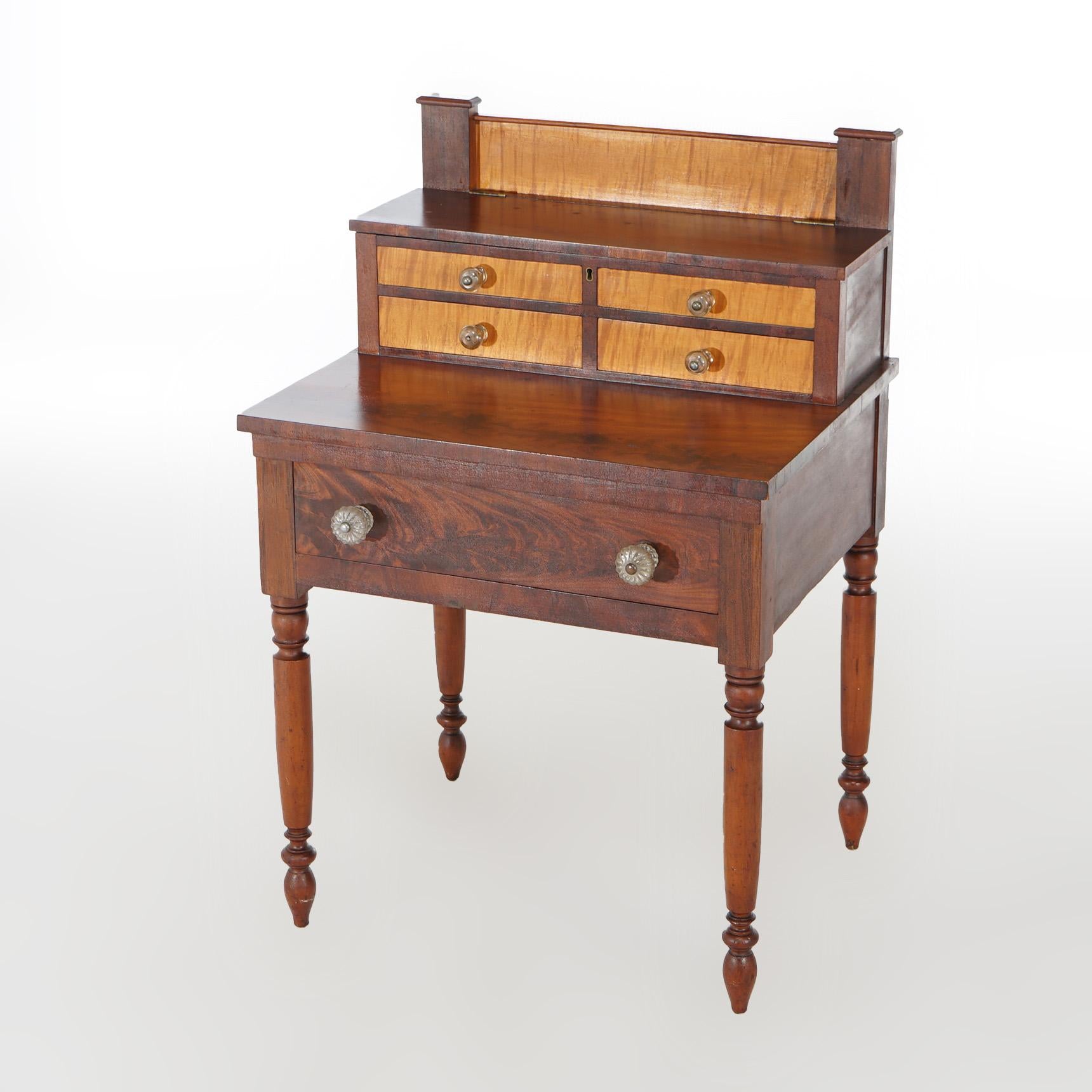 An antique Sheraton sewing stand offers flame mahogany and tiger maple construction with upper lift top compartments having faux drawers and lower small drawers over case with single drawer and raised on turned legs; en verso Gorsch label;