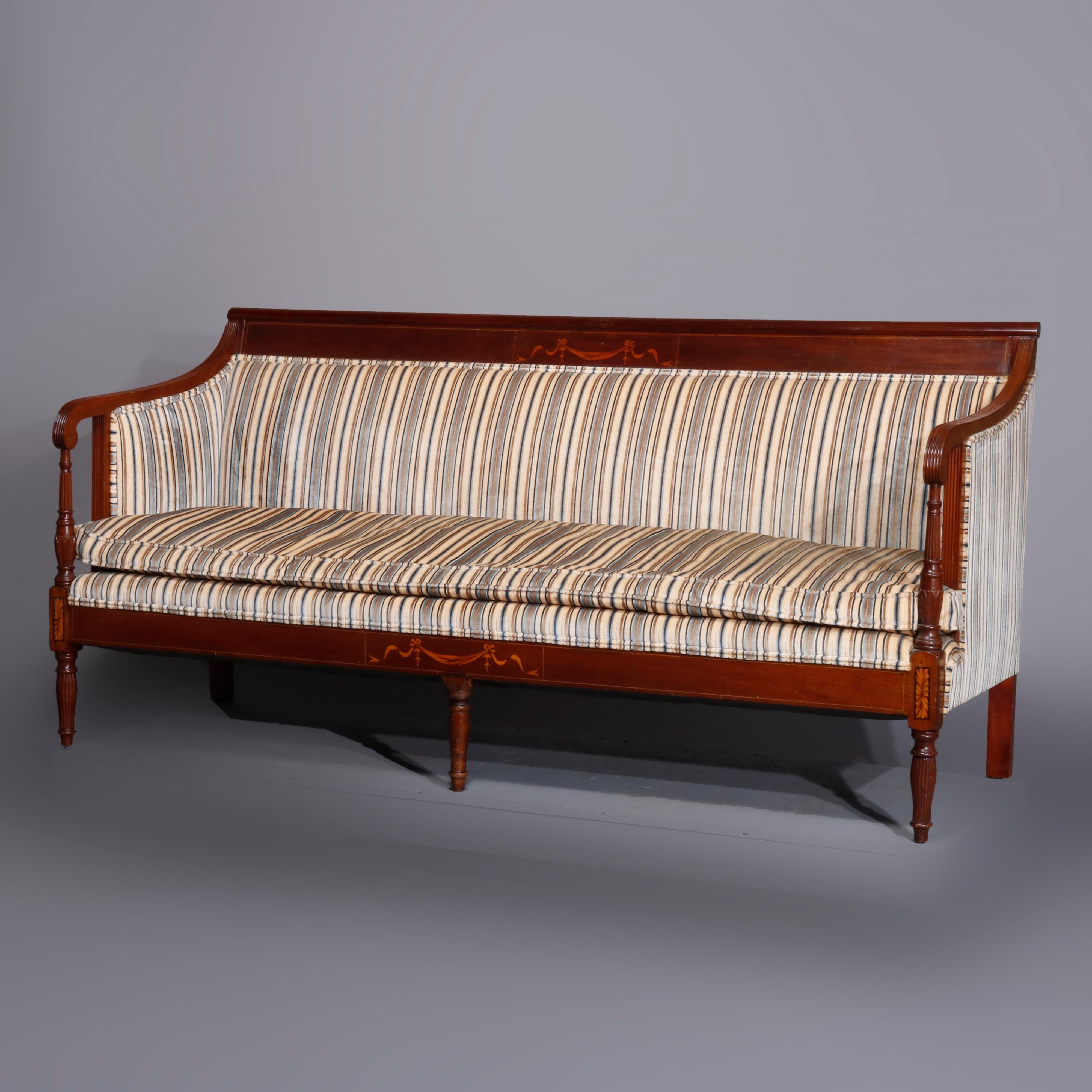 An antique Sheraton sofa offers mahogany construction with scroll back having satinwood inlaid drape and swag over upholstered back and seat with flanking open scroll form arms and satinwood inlaid skirt raised on turned legs, c1820

Measures-