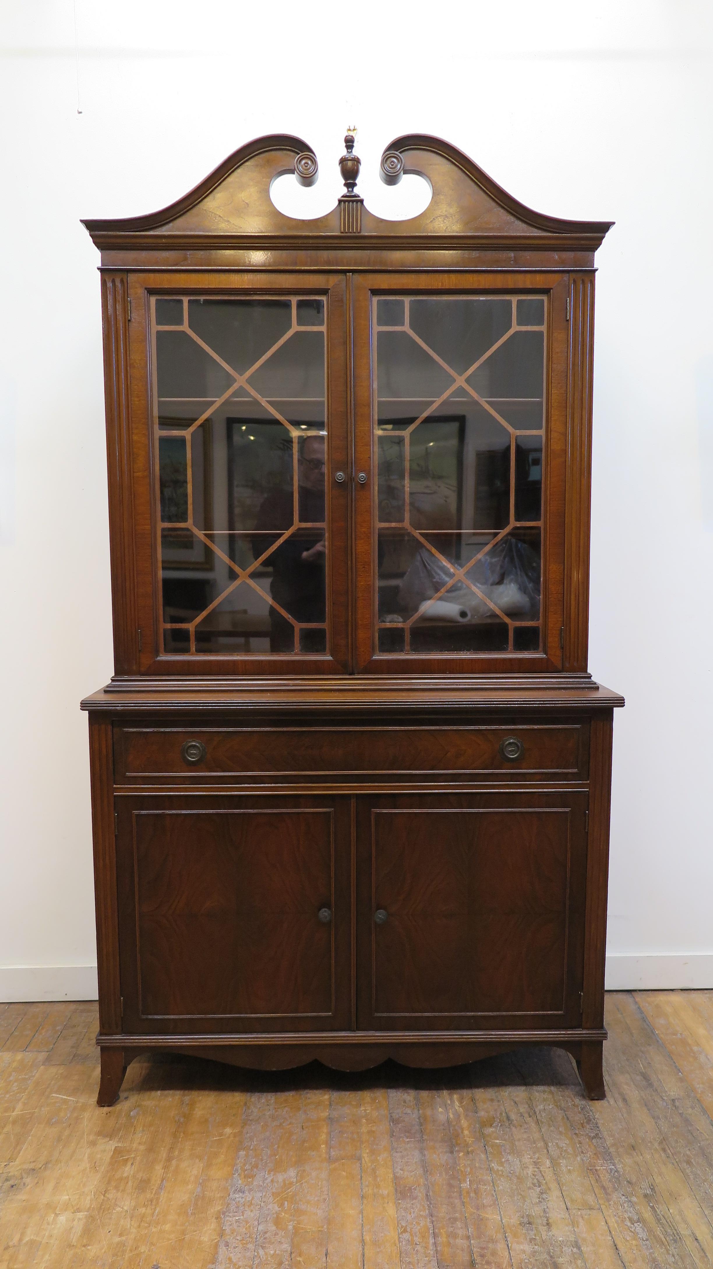 Mahogany Sheraton style display cabinet. Toped with English Georgian cornice detail and center finial having glass doors display case with three shelfs, lower drawer and lower cabinet with two shelfs. Good condition traditional Sheraton Style