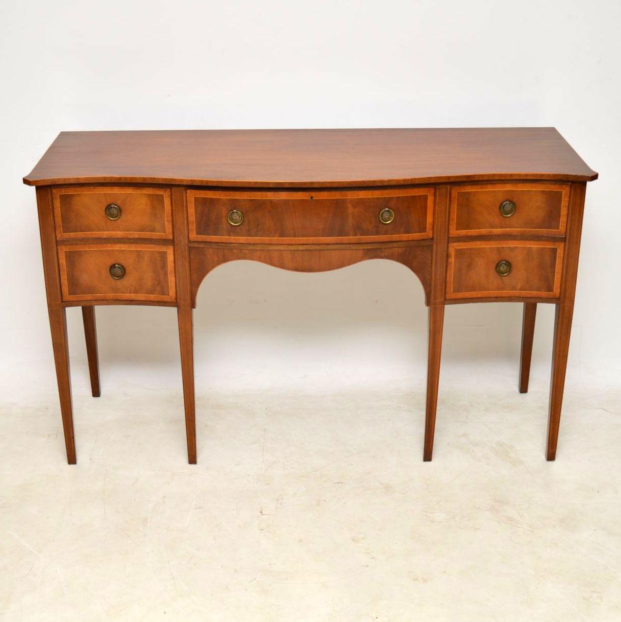 Antique Sheraton style inlaid mahogany sideboard in excellent condition and dating from circa 1930s period.

It has a serpentine shaped front with dummy drawers on either side that are really cupboards and a real drawer in the middle. There’s fine