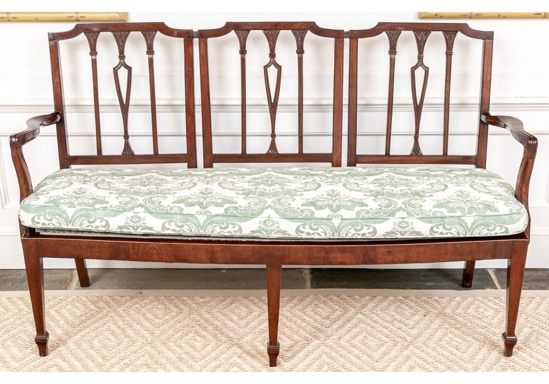 A fine and elegant Sheraton style settee with carved knuckles and a triple chair back with carved Sheraton style lotus flowers. Custom upholstered in a Brunschwig & Fils “Portofino” Woodash/Tarragon green on cream cotton damask. The fabric on the