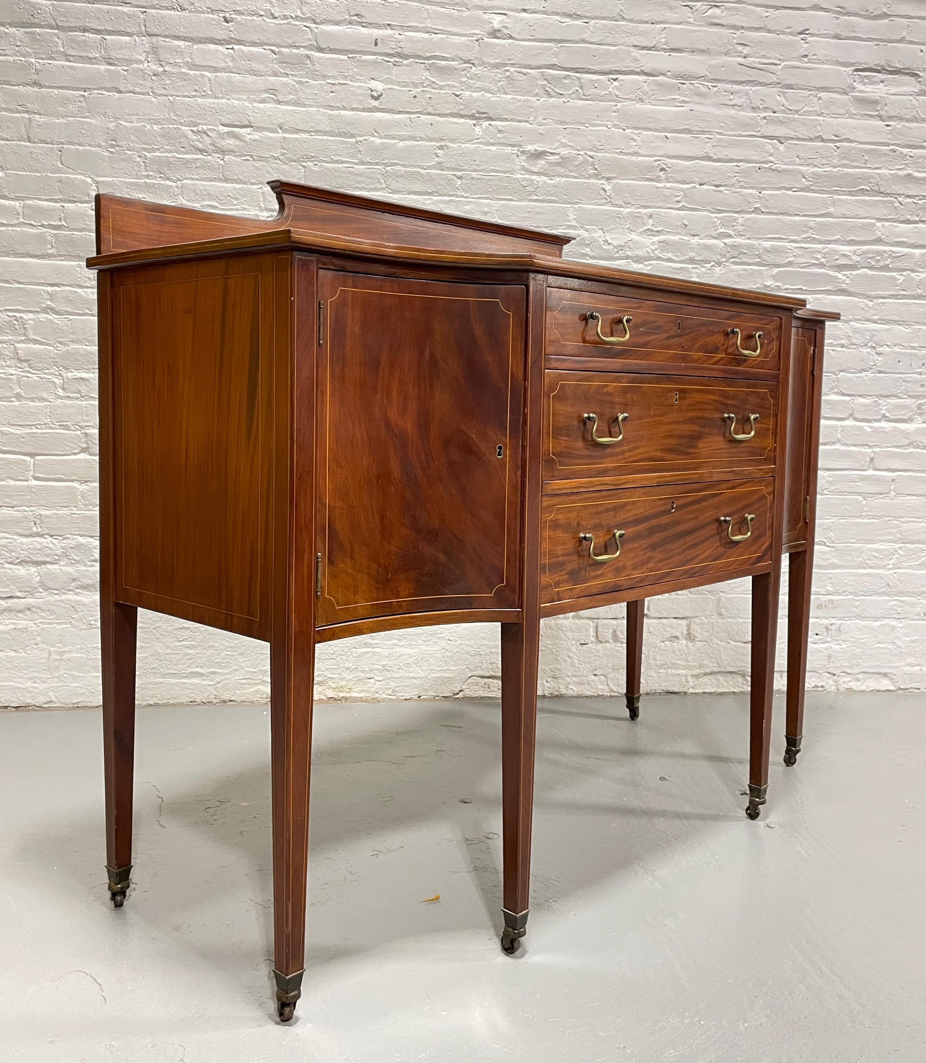 Exquisite Mahogany Sheraton style Sideboard, c. 1910. Stunning flame mahogany wood grains.  This cabinet is raised on 6 square tapered legs with spade feet and castors at the ends. Three deep dovetailed drawers along the front with brass handpulls