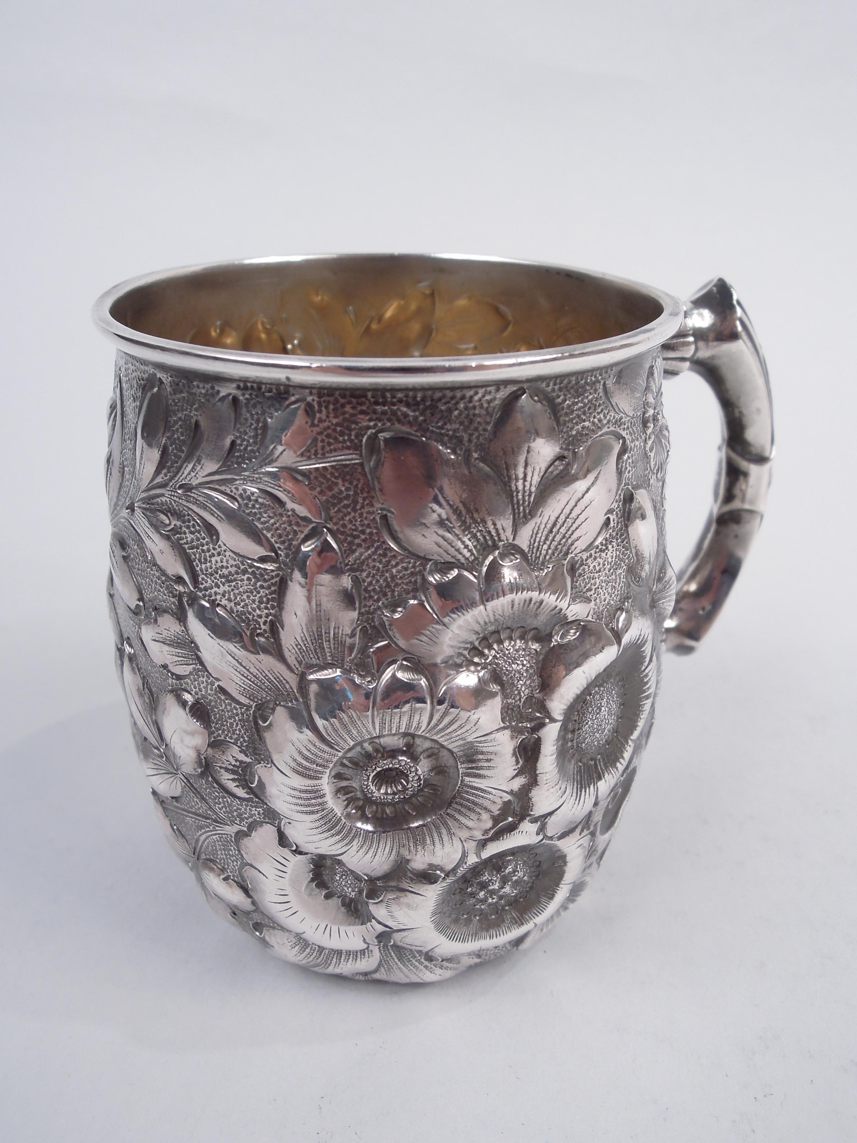 Victorian sterling silver baby cup. Made by George W. Shiebler & Co. in New York, ca 1890. Curved bowl with allover frond and flower repousse on stippled ground. Reeded scroll bracket handle wrapped with applied band decorated with stylized flower