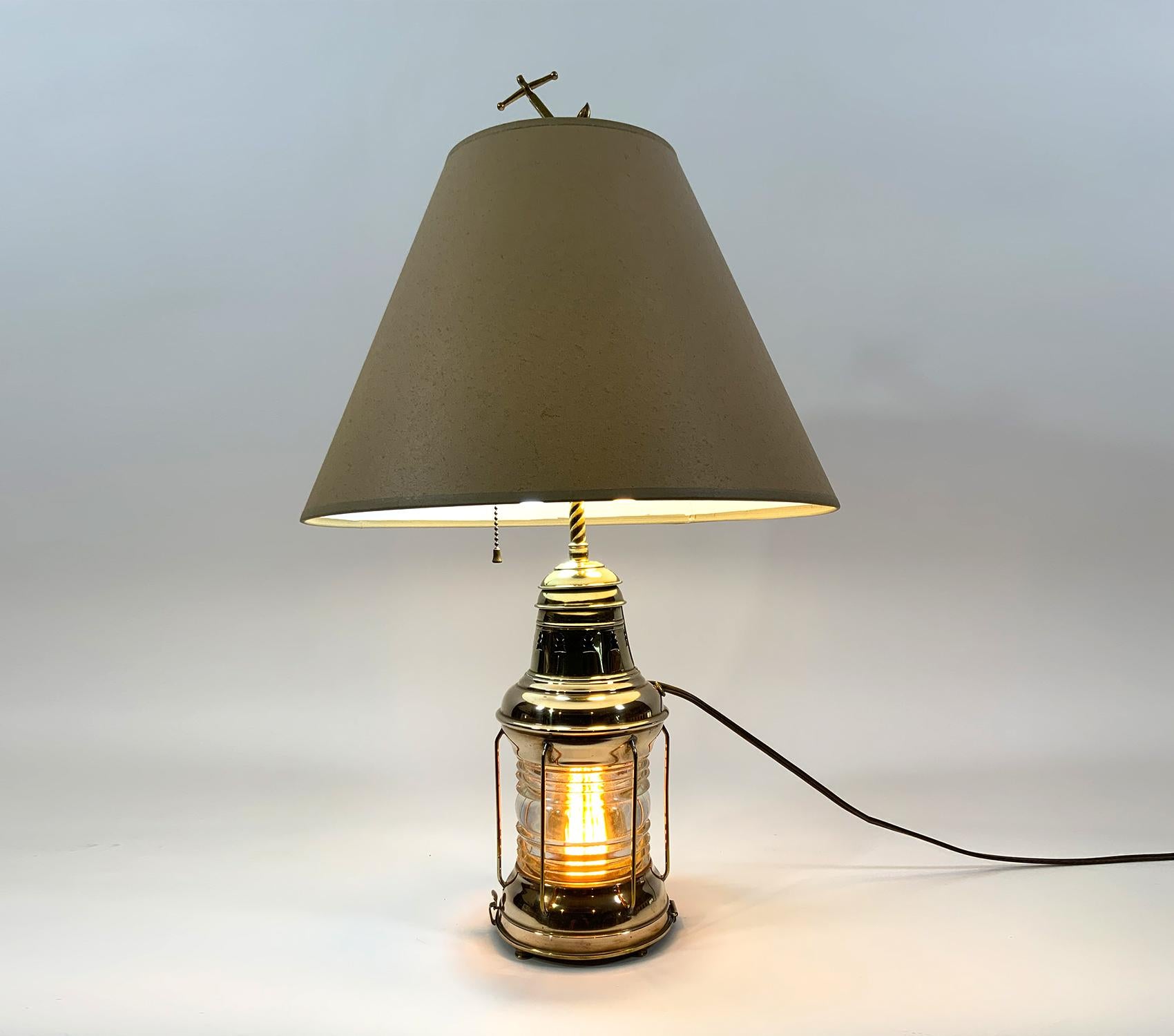 Solid brass ships lantern by Perko, a highly polished and lacquered ships anchor lantern that has been converted to a lamp. With canvas shade. Lantern has a glass Fresnel lens, and protective brass bars. Lamp is wired with electric