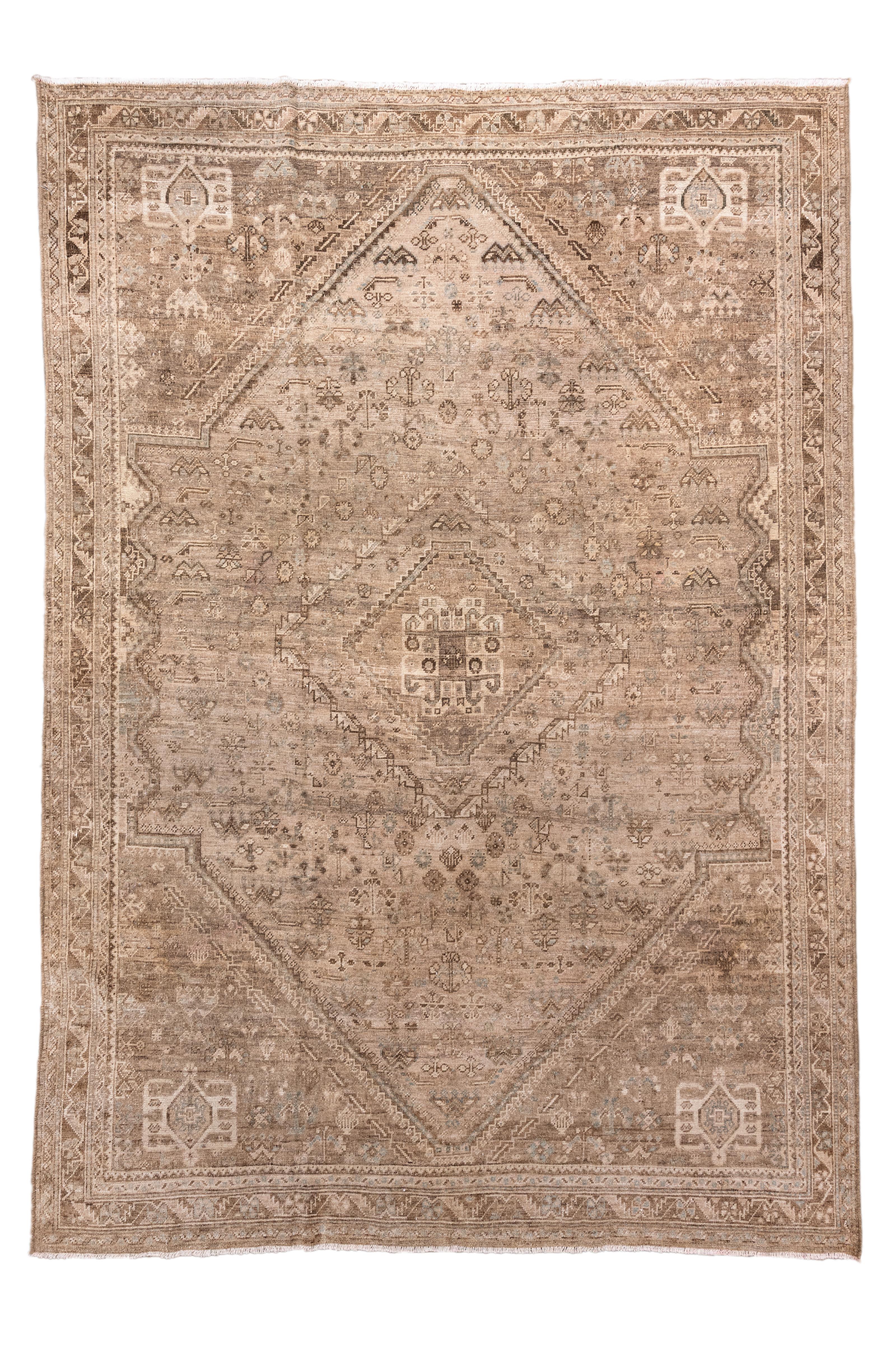 This antique Shiraz rug showcases a striking tribal medallion design in a beautifully subdued, earthy palette of taupe, mocha, ivory, and stone. Woven in the Fars province of southern Persia, this piece exemplifies the regional aesthetic: geometric