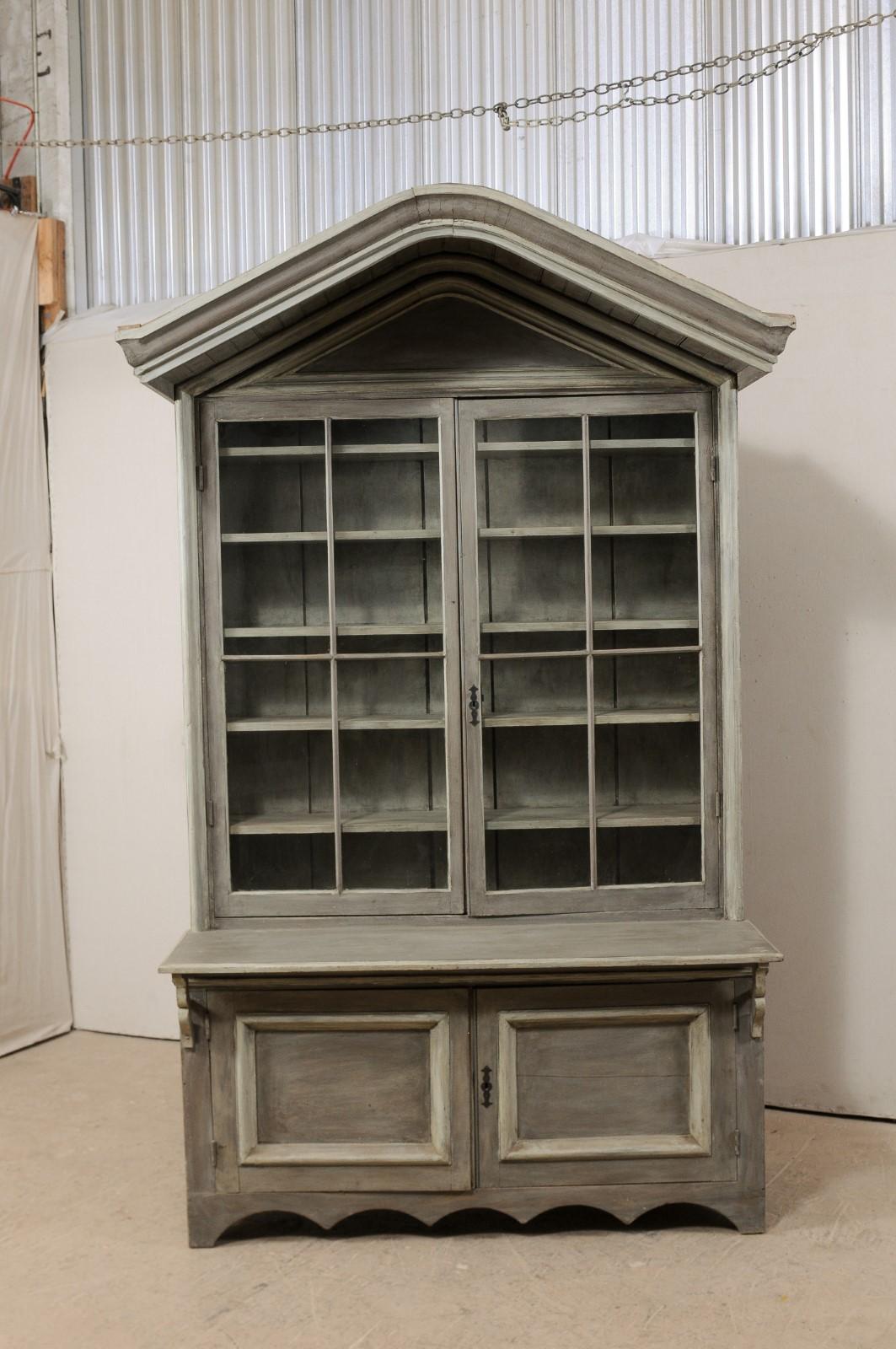 A fabulous early 19th century American shop cabinet with upper glass doors and a pronounced canopy bonnet. This unique antique display and storage cabinet, standing approximately 8.5 feet tall, features an arched bonnet top, which overhangs as a