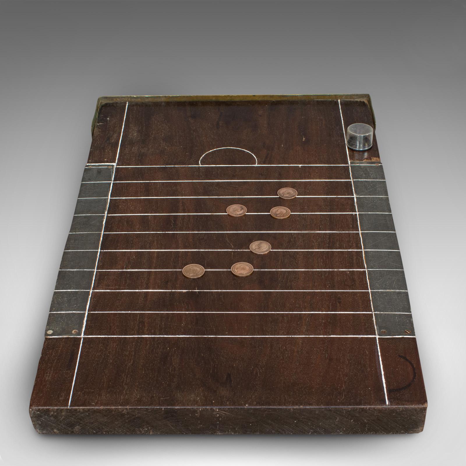 This is an antique shove ha'penny board. An English, mahogany travel gaming table with coins, dating to the late 19th century, circa 1900.

A classic, elegant gaming board 
Displays a desirable aged patina
Rich mahogany hues with fine grain