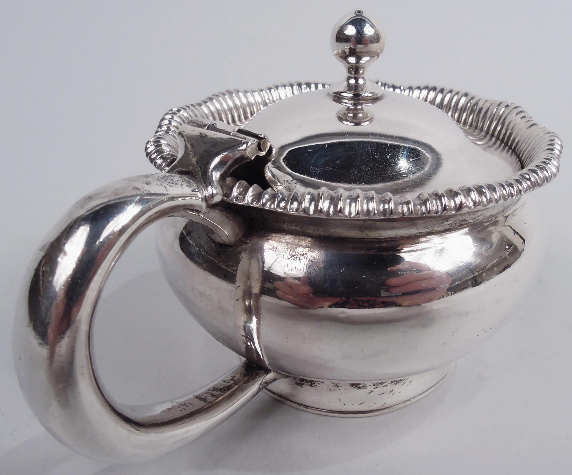 Klassischer amerikanischer Senftopf aus Sterlingsilber, um 1870. Bauchige Schale auf kurzem und gespreiztem Fußring; C.C.-Griff. Aufklappbarer, gewölbter Deckel mit Kugelknauf, eingefasst in einen geschwungenen und gadronierten Mundrand. Gezeichnet