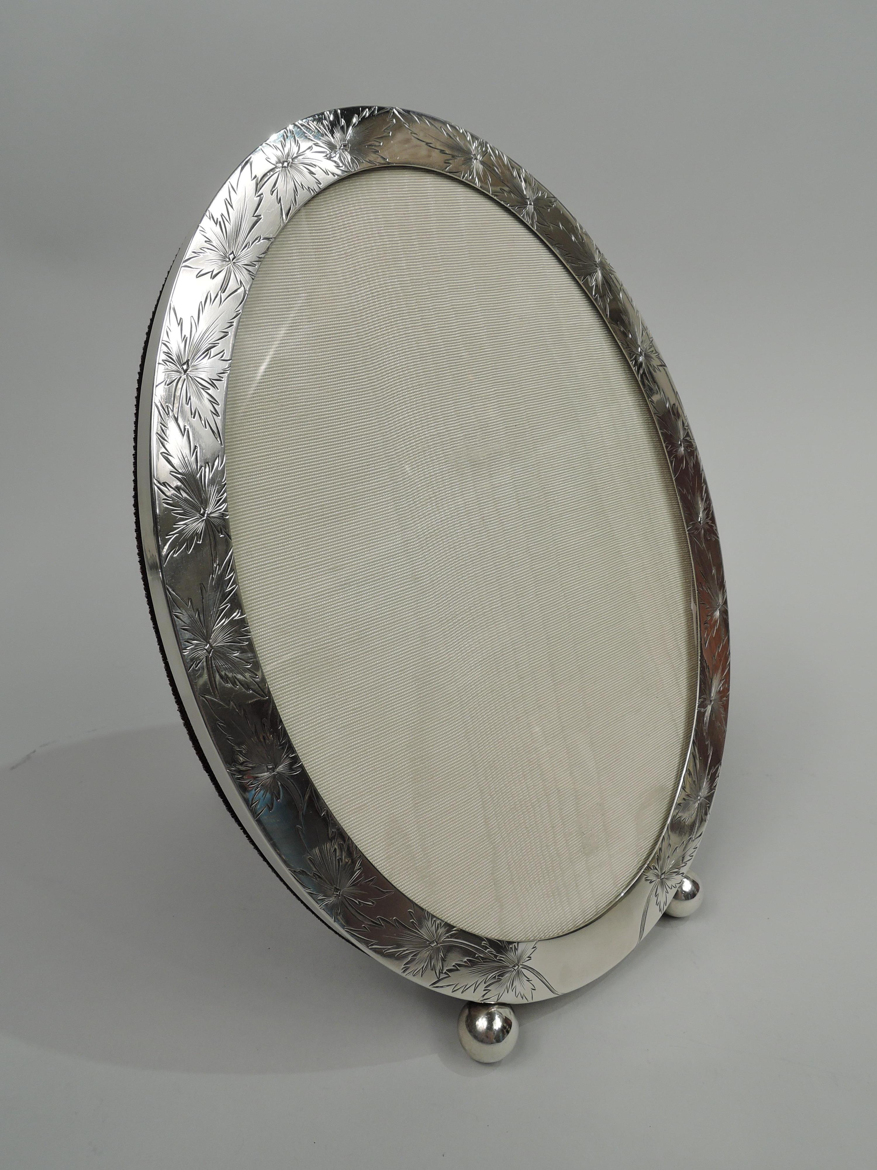 Edwardian sterling silver picture frame. Made by Shreve & Co. in San Francisco, ca 1910. Oval window in same surround; on front engraved ivy leaf garland with spiky tips and reeded stems. Sides plain. Two delightful ball supports. With glass, silk