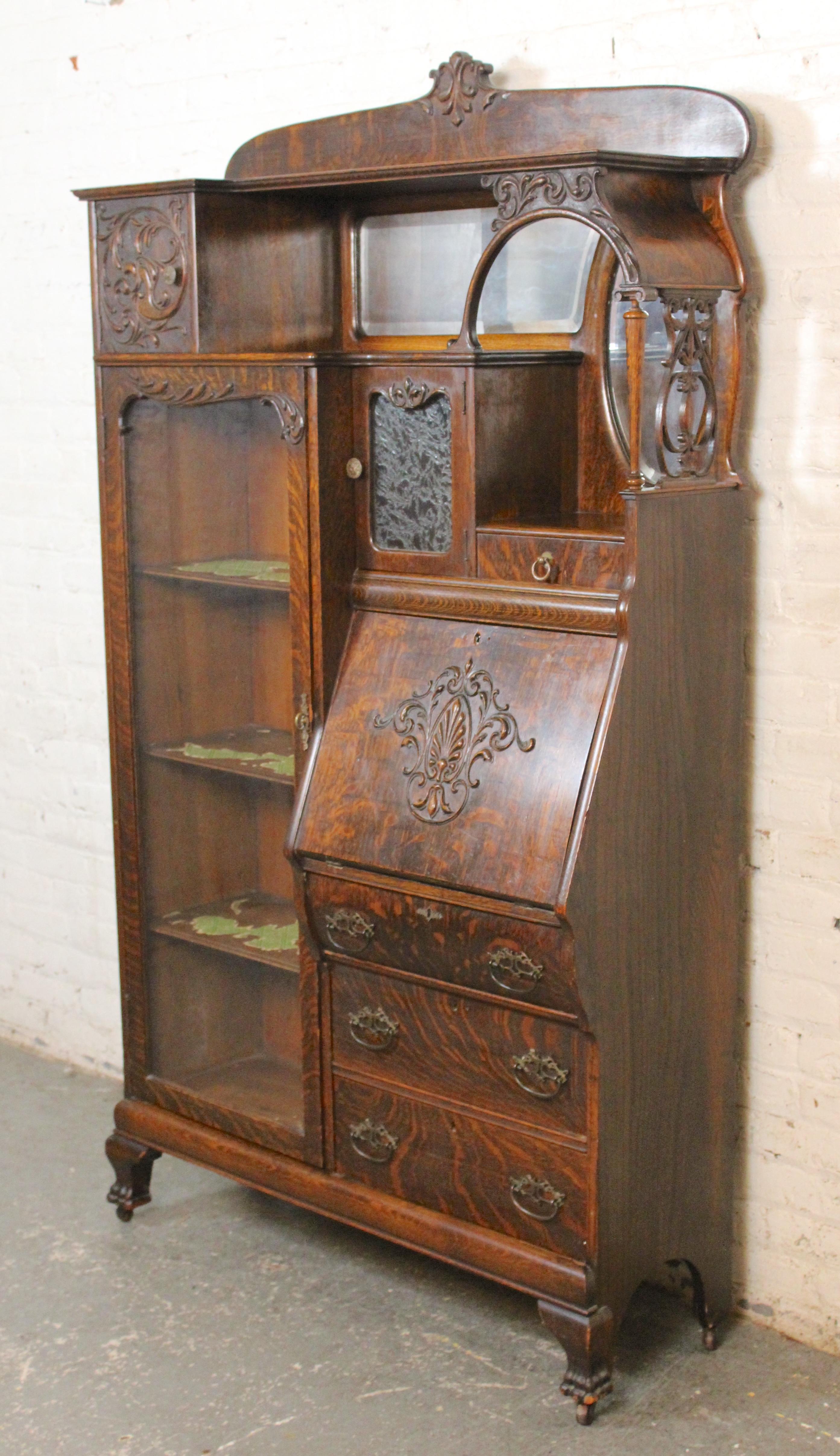 Antique American side by side display and secretary cabinet. Made of beautiful quartersawn oak wood with elaborate sculpted wood embellishments. The display cabinet has three removable shelves, plus small cabinet above. The secretary desk folds down