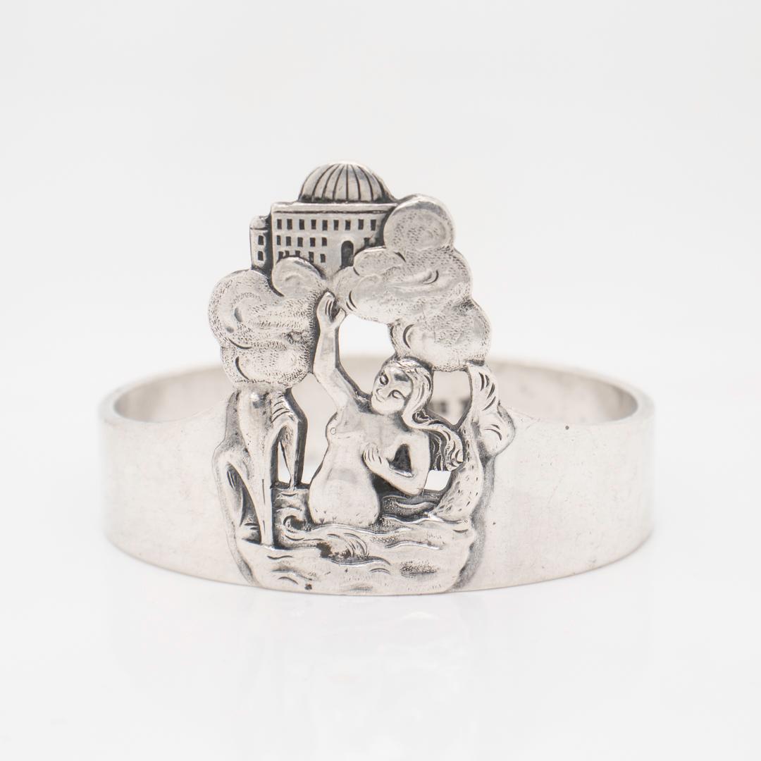 A fine antique Norwegian figural silver napkin ring.

With a cast Mermaid figure in a setting with clouds and building in the background.

Marked 830S for .830 silver fineness.

Monogrammed to the reverse.

Simply a wonderful figural napkin