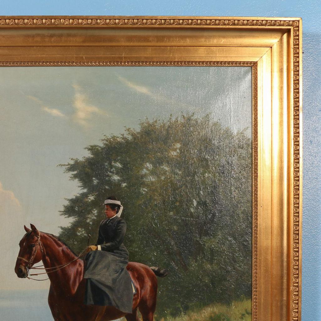 This bright, early 20th century landscape portrays a stylish woman sitting on her bay horse side-saddle in period clothing. The majestic horse and rider stand quietly on a hillside overlooking the ocean. The painting is mounted in a gilt wood frame