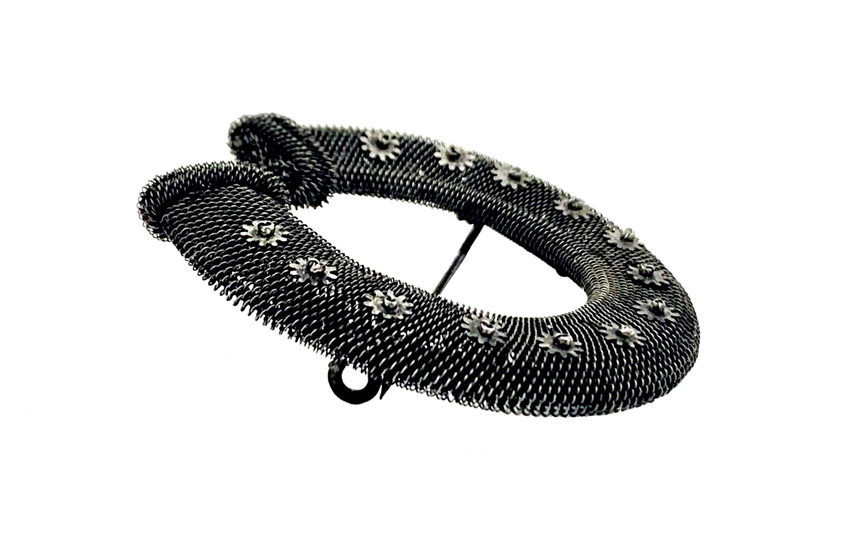  The brooch in the shape of a horseshoe was handcrafted out of woven iron thread. The horseshoe is made out o iron mesh and decorated with twelve little flower heads made out of cut steel. Each of the twelve flowers is secured by twelve facetted