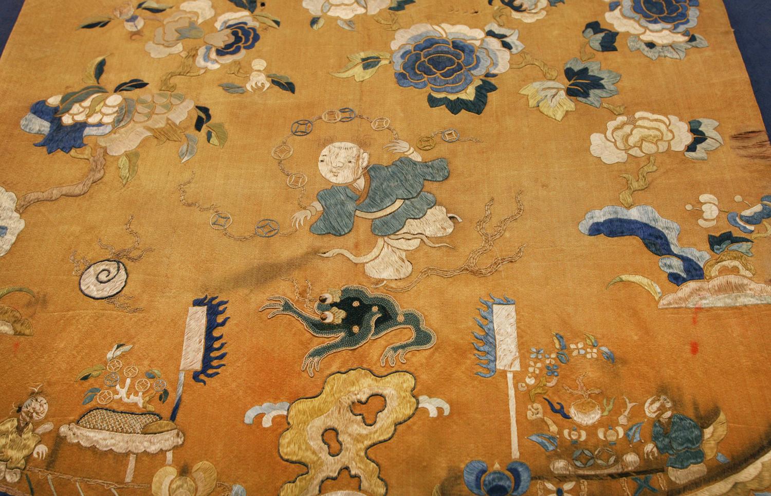 Il s'agit d'un petit textile chinois ancien en soie tissé au début du 20e siècle, vers 1900. Il mesure 50 x 47CM. Son design est centré sur un homme qui tient des talismans traditionnels chinois dans une bande de nuages et est entouré d'arbres avec