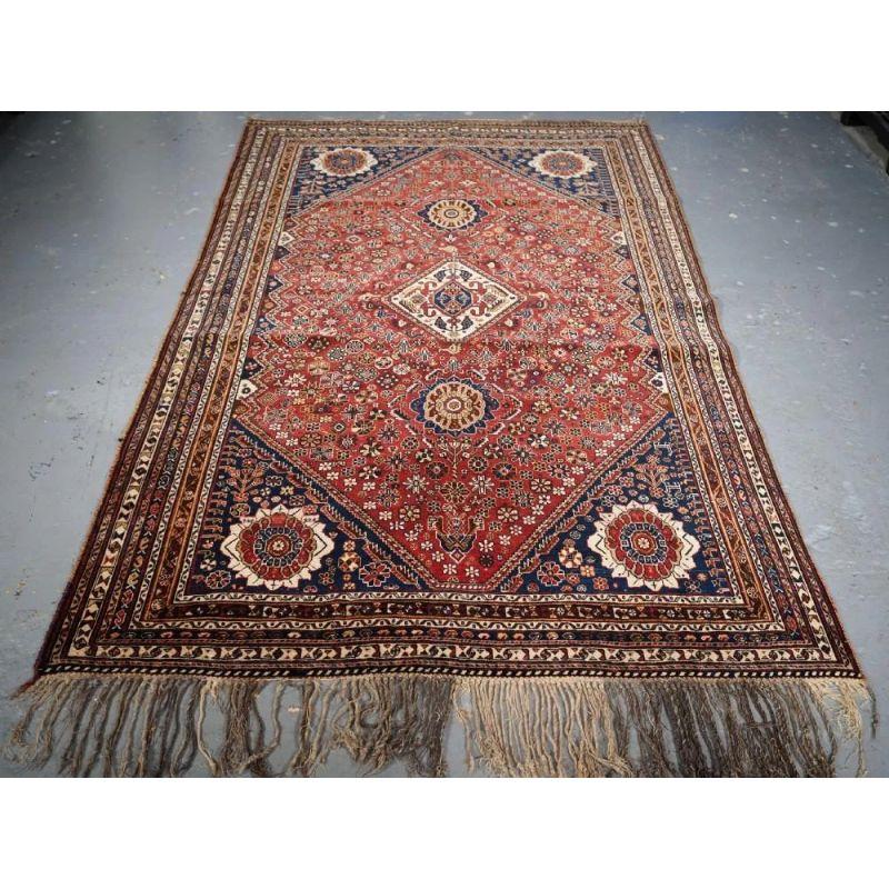 This rug has three small medallions on a soft madder red ground. The four indigo blue corners each contain a sunburst design. The central medallion contains the Qashqai tribal emblem, it is surrounded by small well drawn chickens. The field is