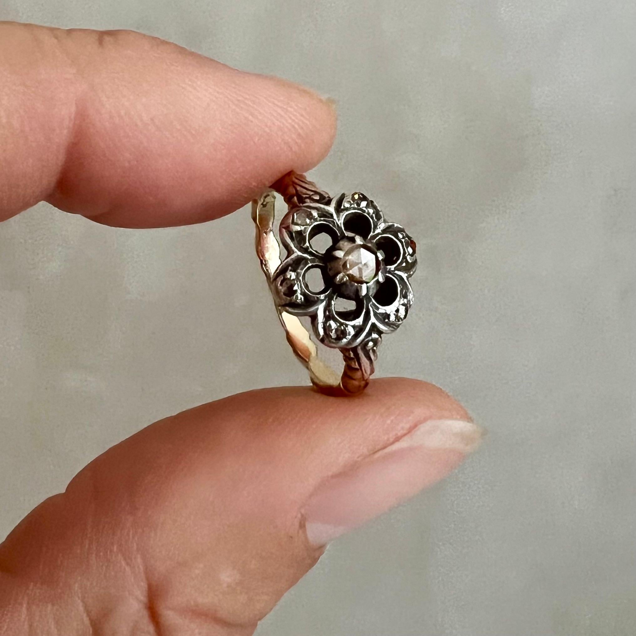 Questo squisito anello antico è un esempio senza tempo di eleganza e maestria, che combina l'argento e l'oro 14K in un design meravigliosamente armonioso. La parte anteriore dell'anello ha la forma di un fiore delicato, con una struttura in argento
