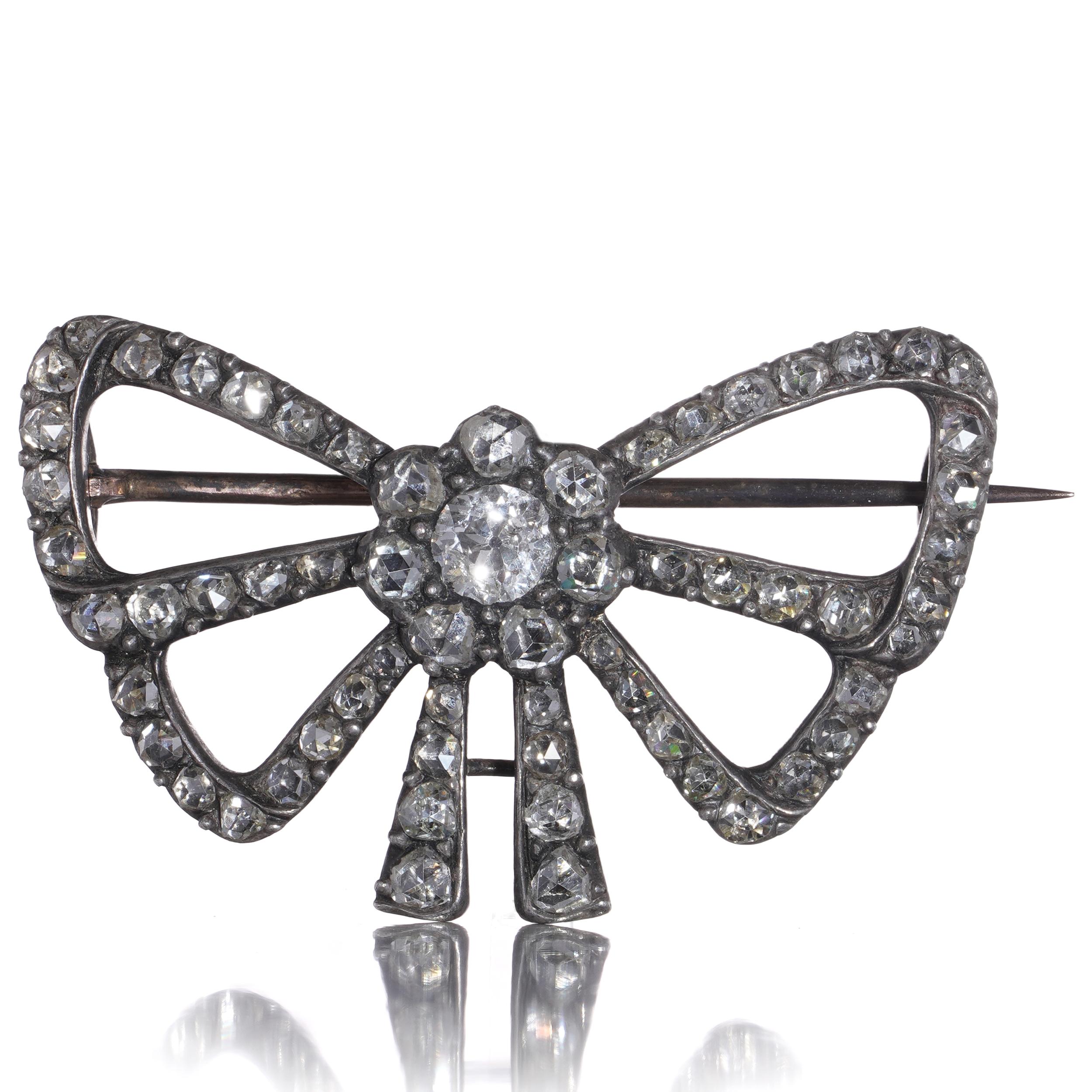 A charming antique bow brooch, finely crafted in silver over 18kt yellow gold and set with an array of 62 diamonds. At the centre lies a prominent old European-cut diamond, surrounded by a cluster of rose-cut stones, all pavé-set in a sculptural