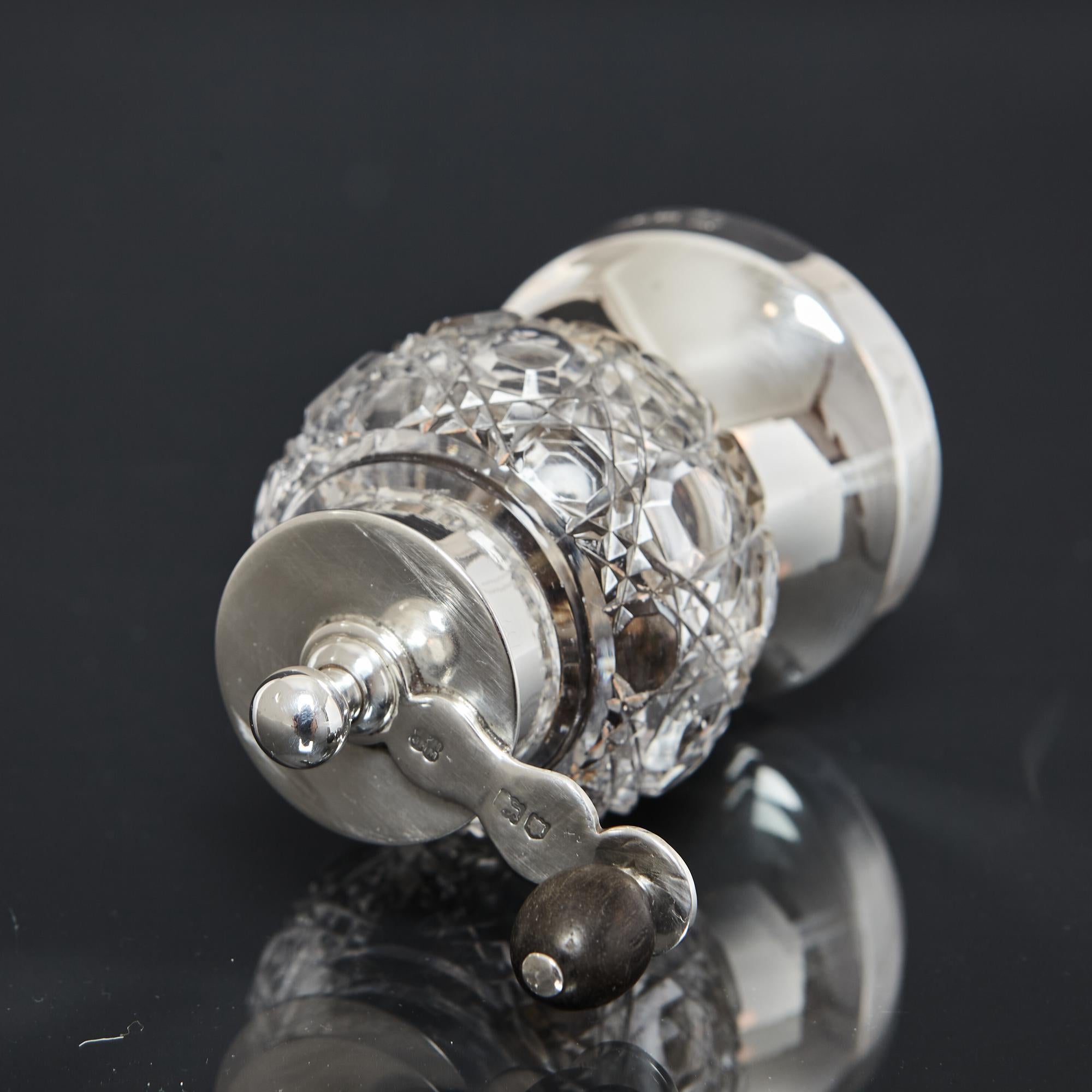 A silver-mounted pepper mill with a glass body, hand cut with a hobnail and diamond pattern, and fitted with a crank handle that is attached to the excellent Peugeot grinding mechanism. The handle has an ebony grip and a ball-shaped finial. This