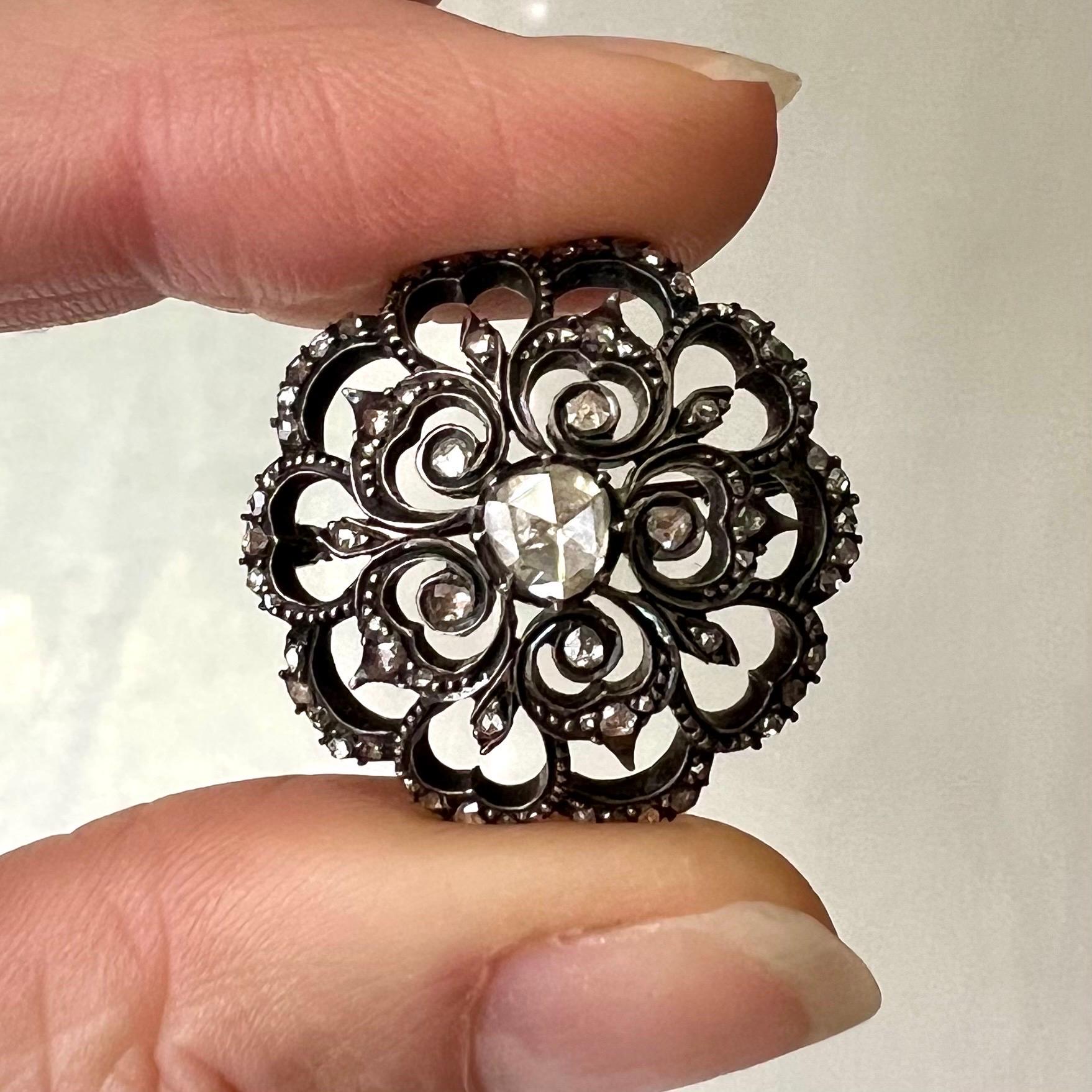 This exquisite antique brooch is a stunning example of timeless elegance, crafted in silver and 14 karat gold with a captivating round floral design. The brooch is adorned with an array of sparkling rose-cut diamonds, each meticulously set to