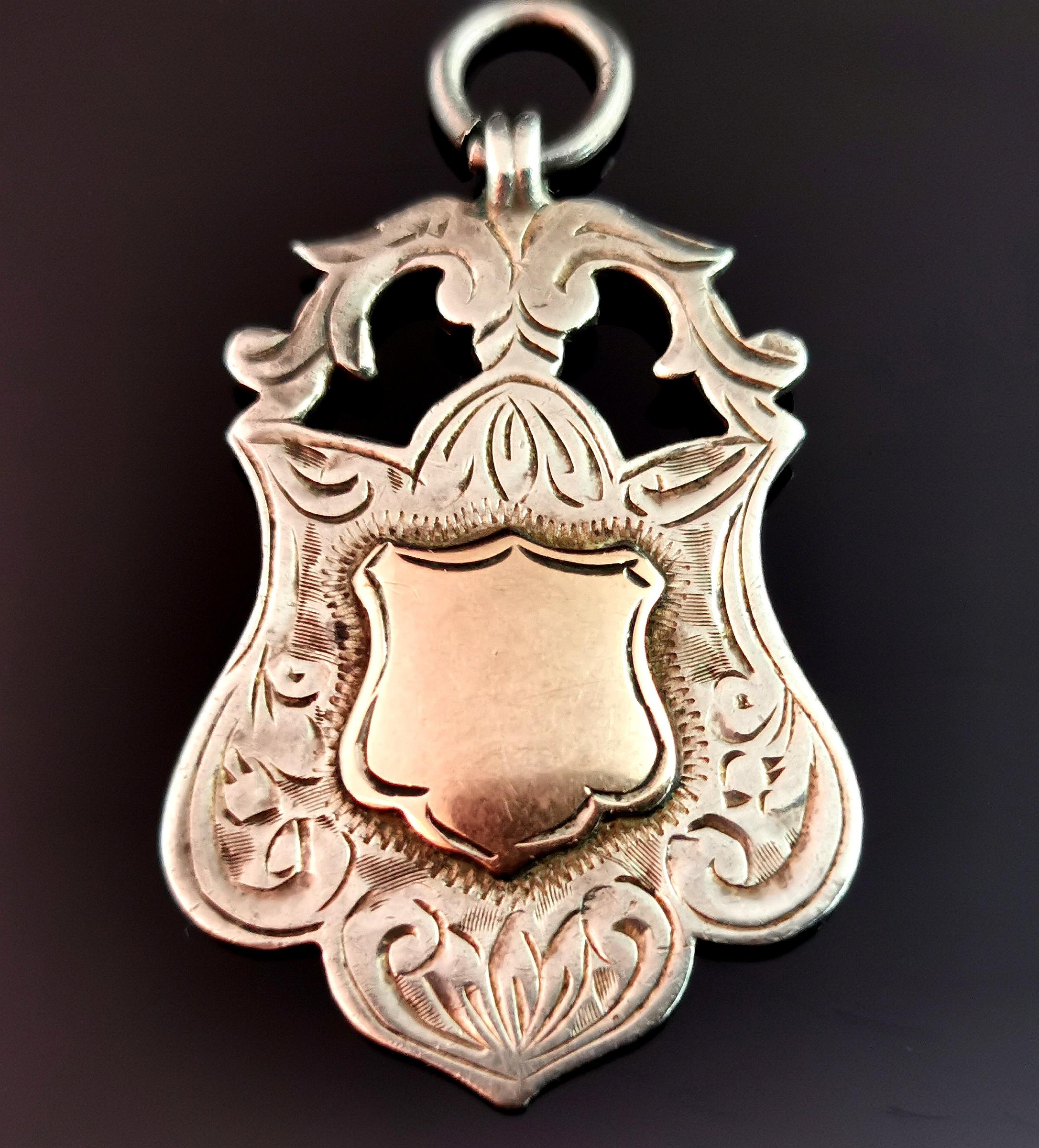 An attractive antique, Art Deco sterling silver and Rose gold shield fob.

A nice heavy fob with a decorative engraved shield design and a 9kt Rose gold cartouche to the centre, this has not been monogrammed or engraved so could be personalised if