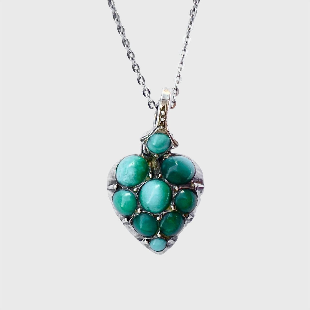 Ciondolo a forma di cuore in argento 935 e turchese su una catena in argento. La catena è di data successiva al ciondolo. Abbiamo sostituito la chiusura.

La catena misura 46,8 cm e il ciondolo misura 1,2 cm di larghezza massima.

Si tratta di