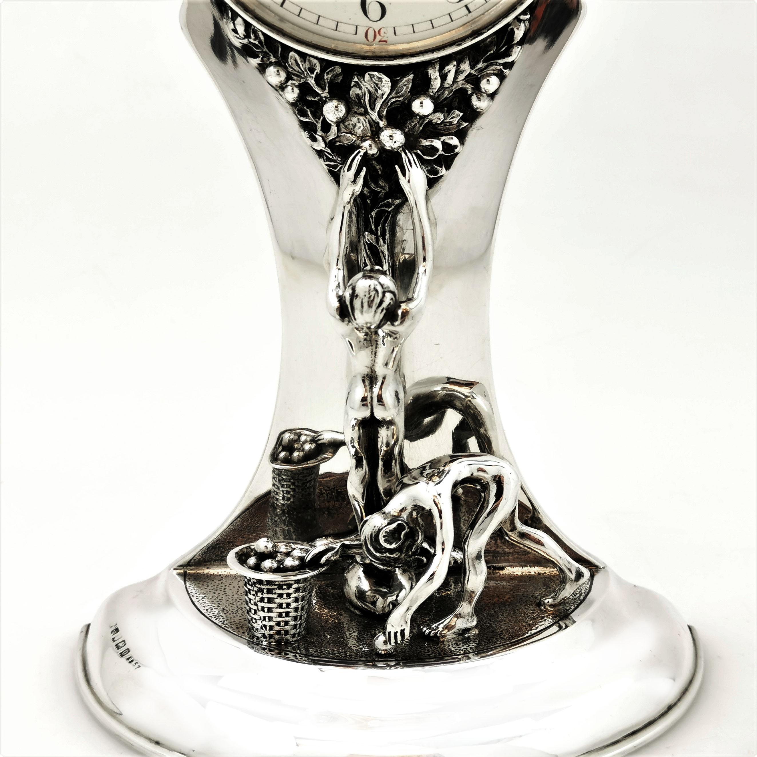 A magnificent Antique Sterling Silver Table Clock decorated with an impressive Art Nouveau design showing a Tree of Life design with two figures picking a basket of apples from the tree. This design flows up the central column from the half circular