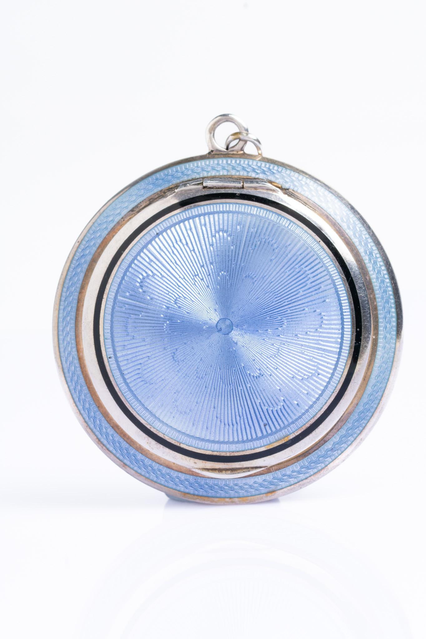 Questo bellissimo ciondolo Art Deco in argento e smalto guilloché azzurro è stato realizzato molto probabilmente in Austria o in Svizzera ed è datato 1921. Il coperchio anteriore di questo fantastico pezzo presenta una decorazione in smalto