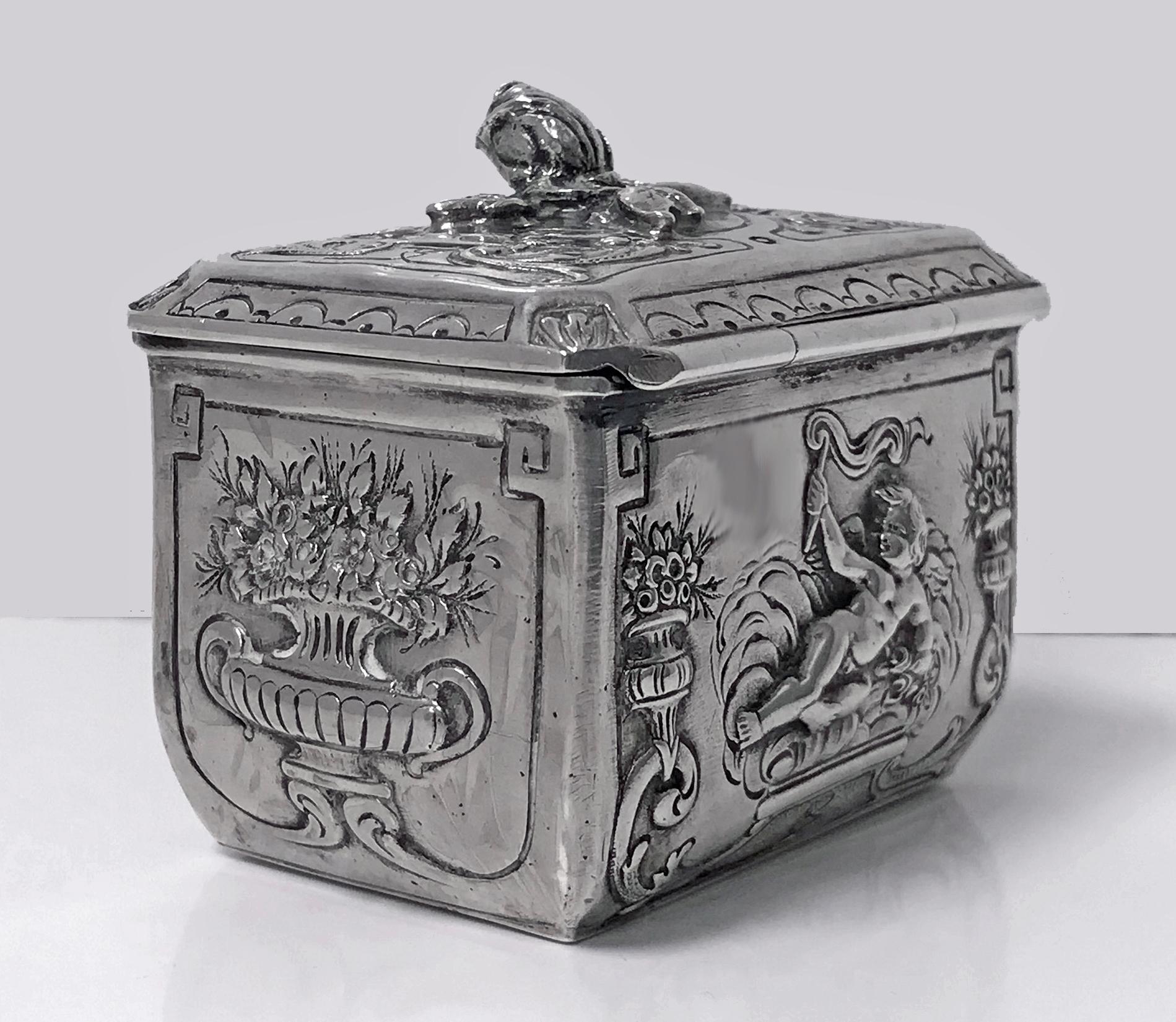 Antique silver box, Germany, circa 1900. The box in the form of a small casket, all with embossed raised decorative depictions of winged angels cupids, foliage and classical urns against, the hinged cover with an applied raised foliage closed petal