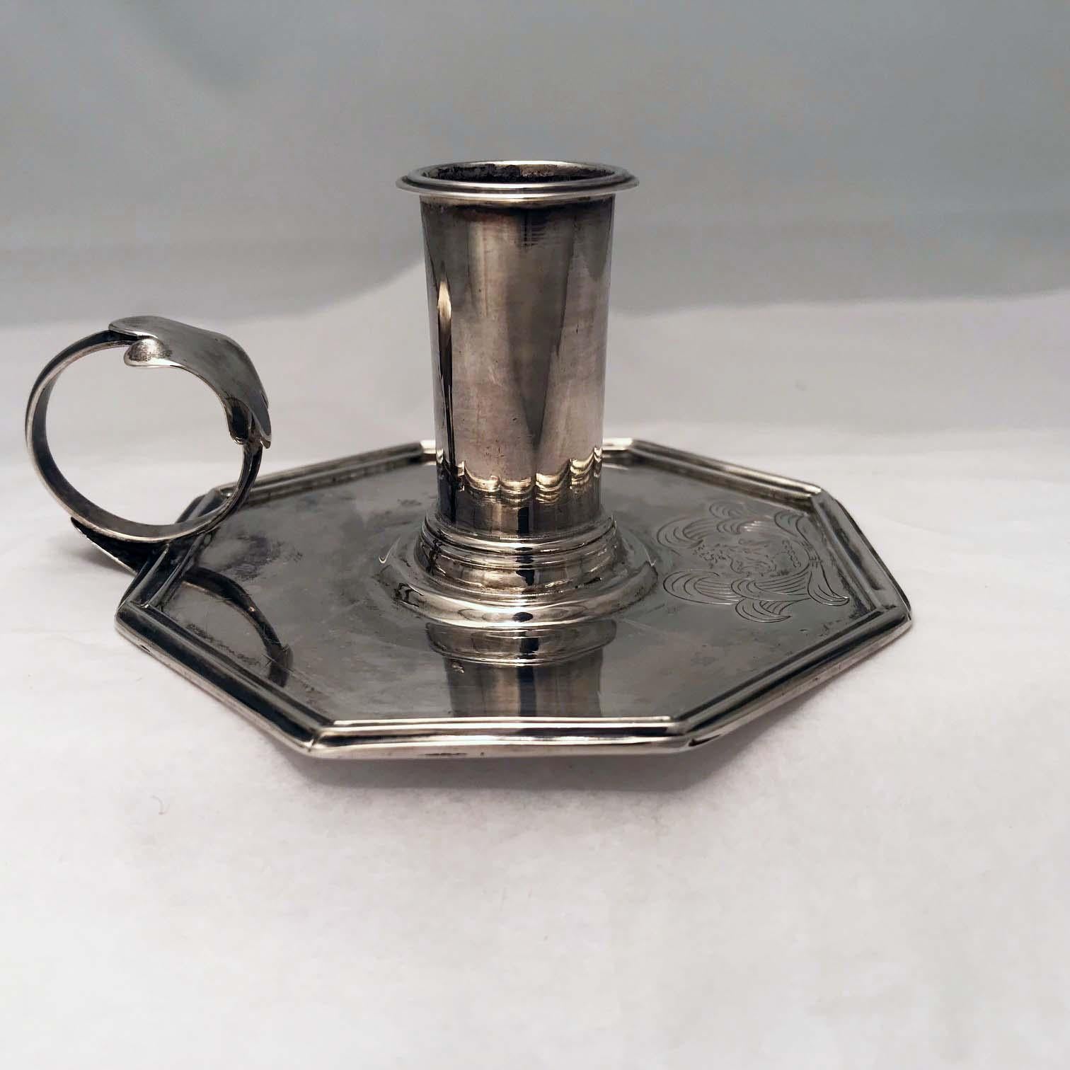 This small silver chamberstick, though of uncertain origin, is very much in the style of the early part of the eighteenth century. It has a pleasingly simple form, The reeded octagonal base is centered by the candlestick proper and has an applied