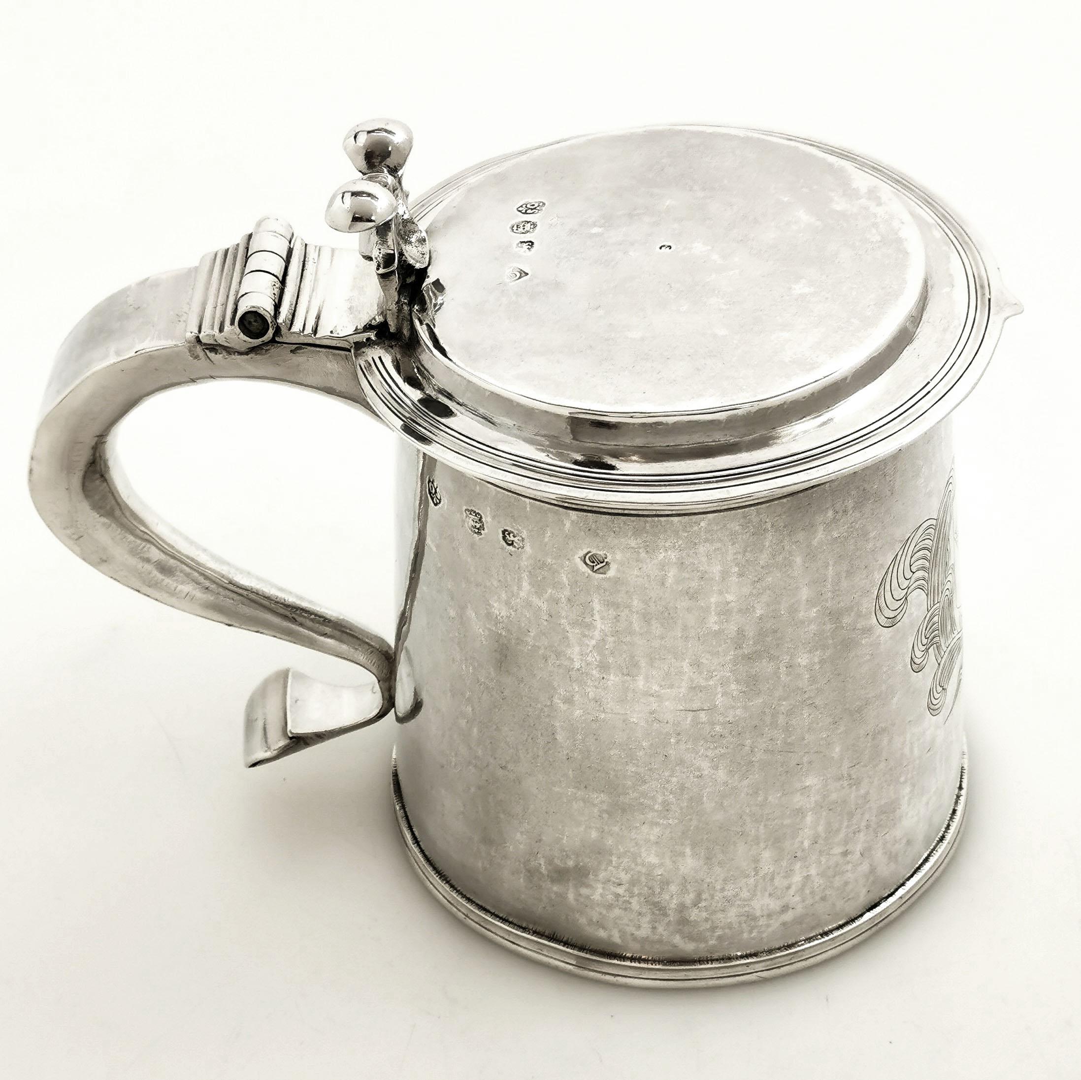 A magnificent Antique Charles II sterling Silver Lidded Tankard. This Tankard has a slight tapered straight sided form with a hinged flat lid. The Tankard features a large engraved crest opposite a substantial scroll handle and a shaped thumb piece