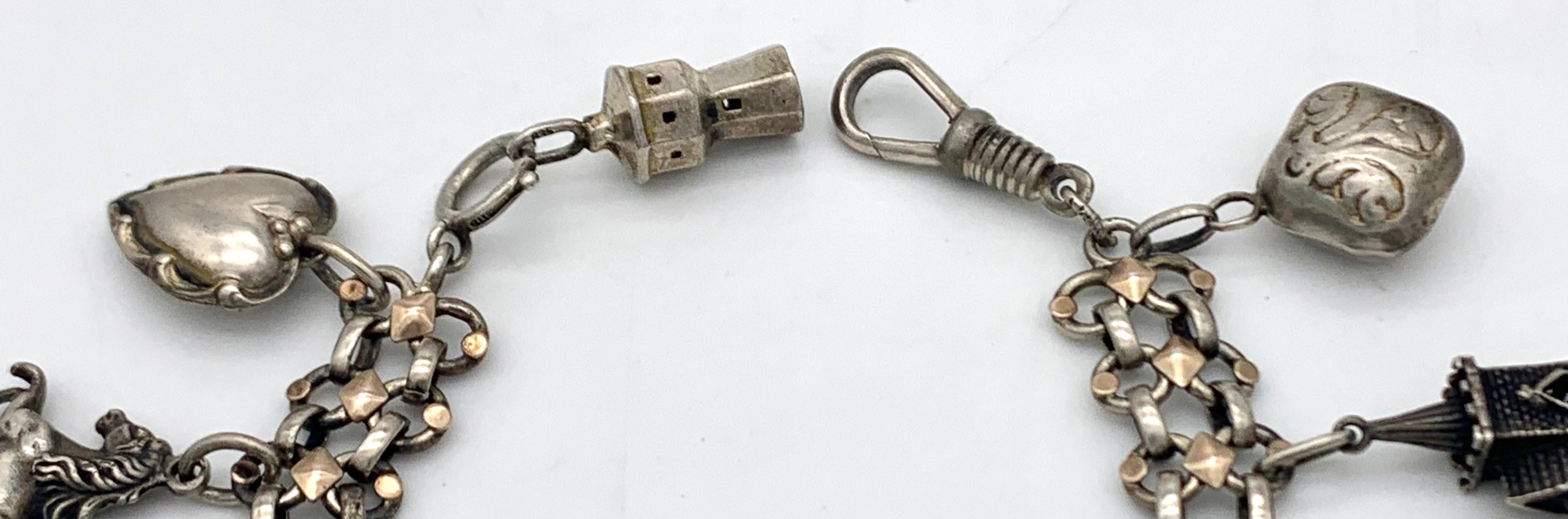 This delightful Bel Époque charm bracelet features nine unusual silver charms on a wide silver link bracelet. The bracelet is decorated with silver gilt elements. The charms are: a lighthouse, a heart, a horse, a box with a lid that reveals a devil