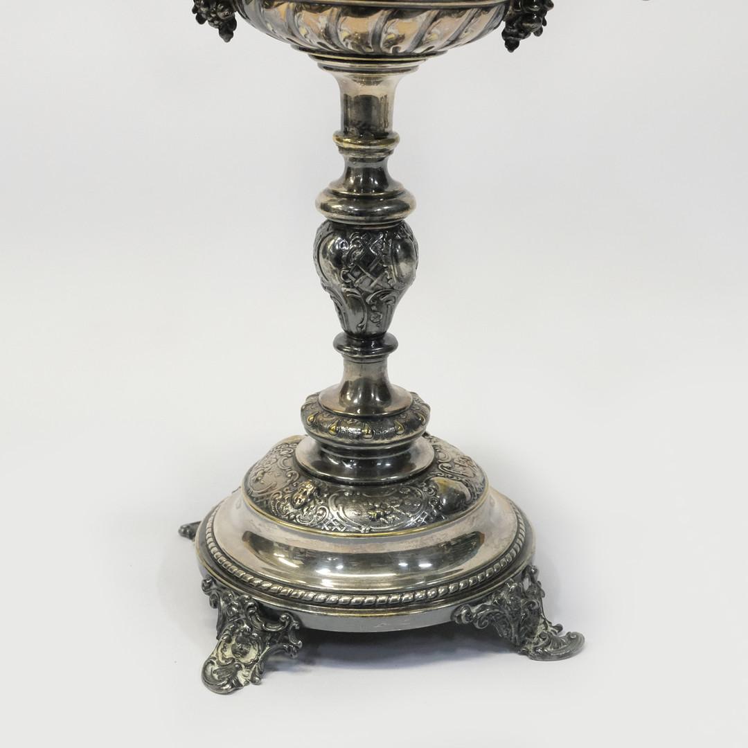Conjunto de objetos decorativos de mesa de comedor que incluye una taza de plata antigua, una taza decorativa para fruta o azucarero con pie, y un par de portavelas de plata prensada, fundida y cincelada. Circular, pies curvados con bisagra. sin