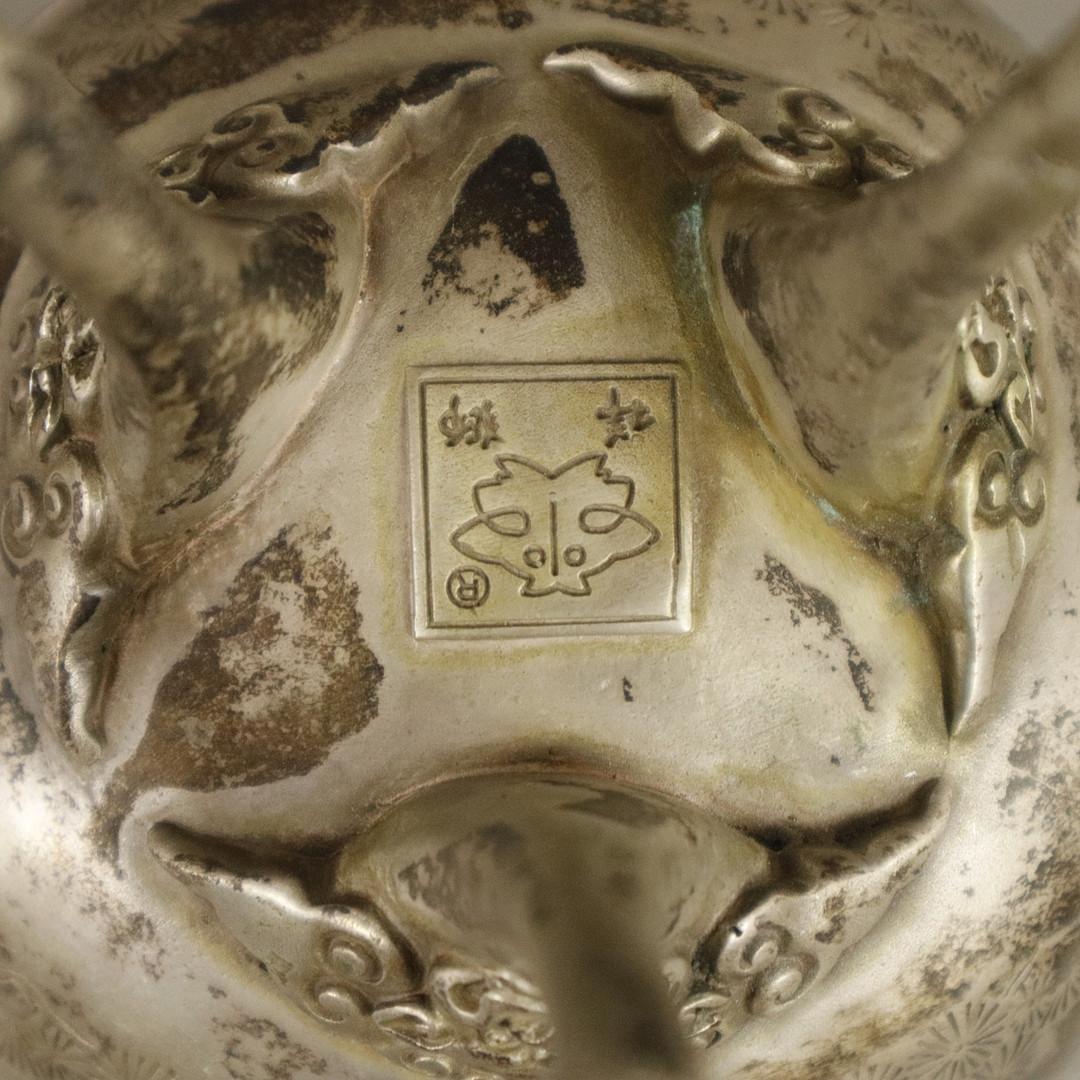 Taza de plata antigua o taza decorativa japonesa, prensada, fundida y cincelada. Pies circulares y curvados con bisagras. Comprobado con la prueba de rayado.
Decorado con motivos de pavos reales en relieve, asas laterales de animales míticos y