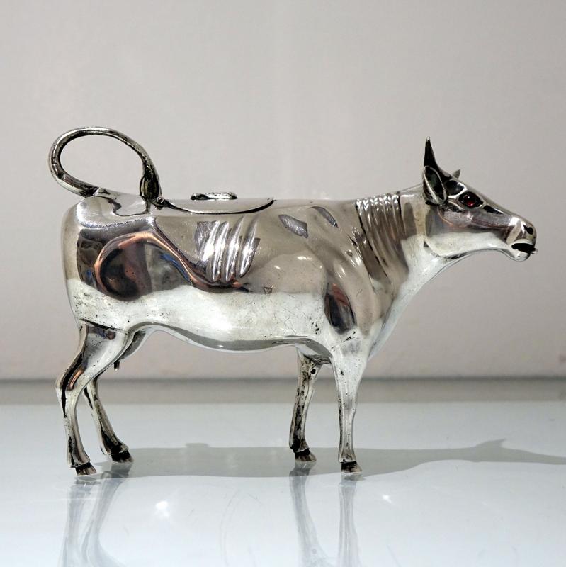 A beautiful 19th century silver Dutch cow creamer with realistic detailing throughout and elegant red stone set eyes for highlights. The lid is hinged and crowned with an insect finial which then brings the “shooing” tail (handle) into action to