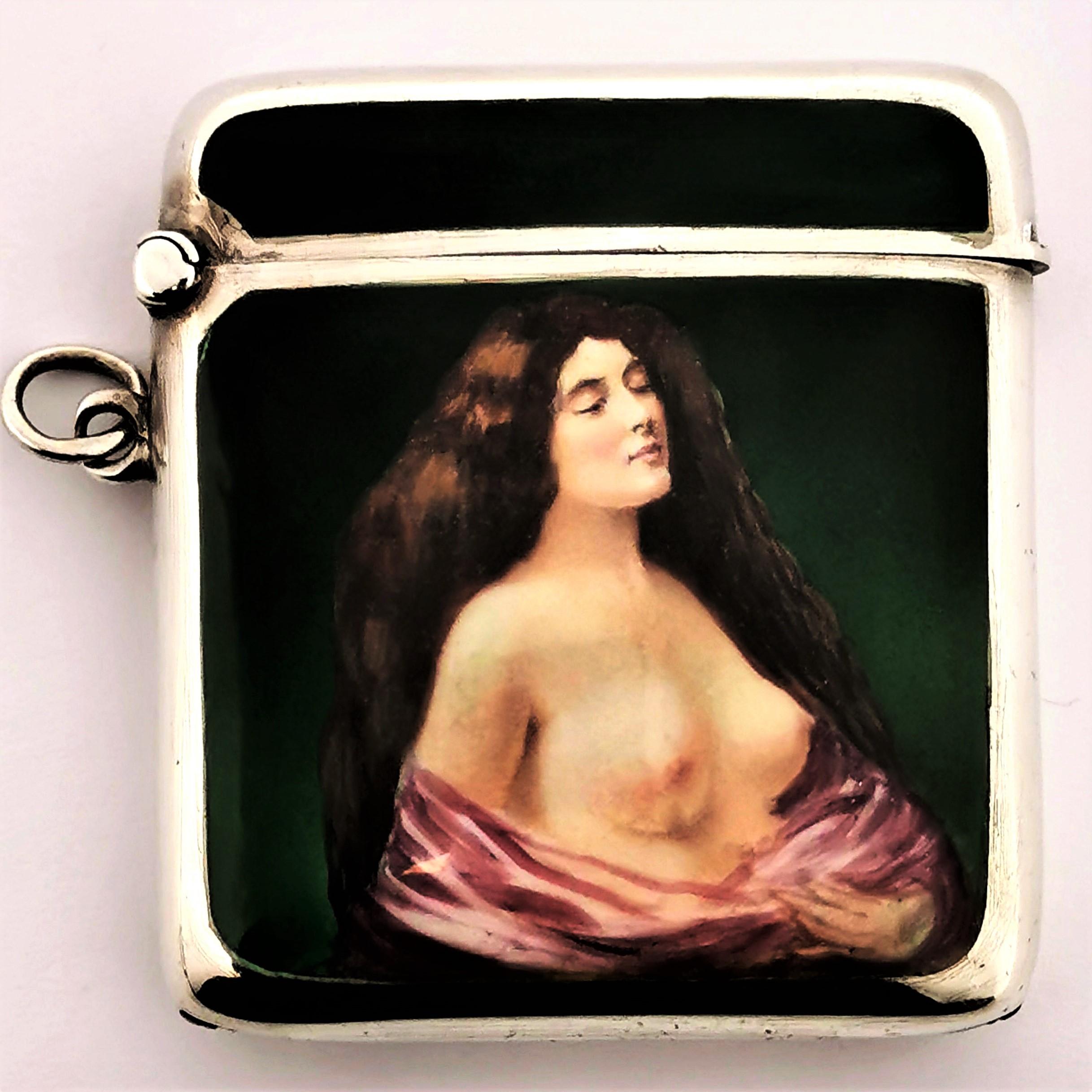 A lovely antique silver and enamel vesta case / match holder. This Vesta has a richly colored enameled image on the front showing a nude woman wrapped in pink fabric against a rich green background. The case is polished silver and it has a hinged