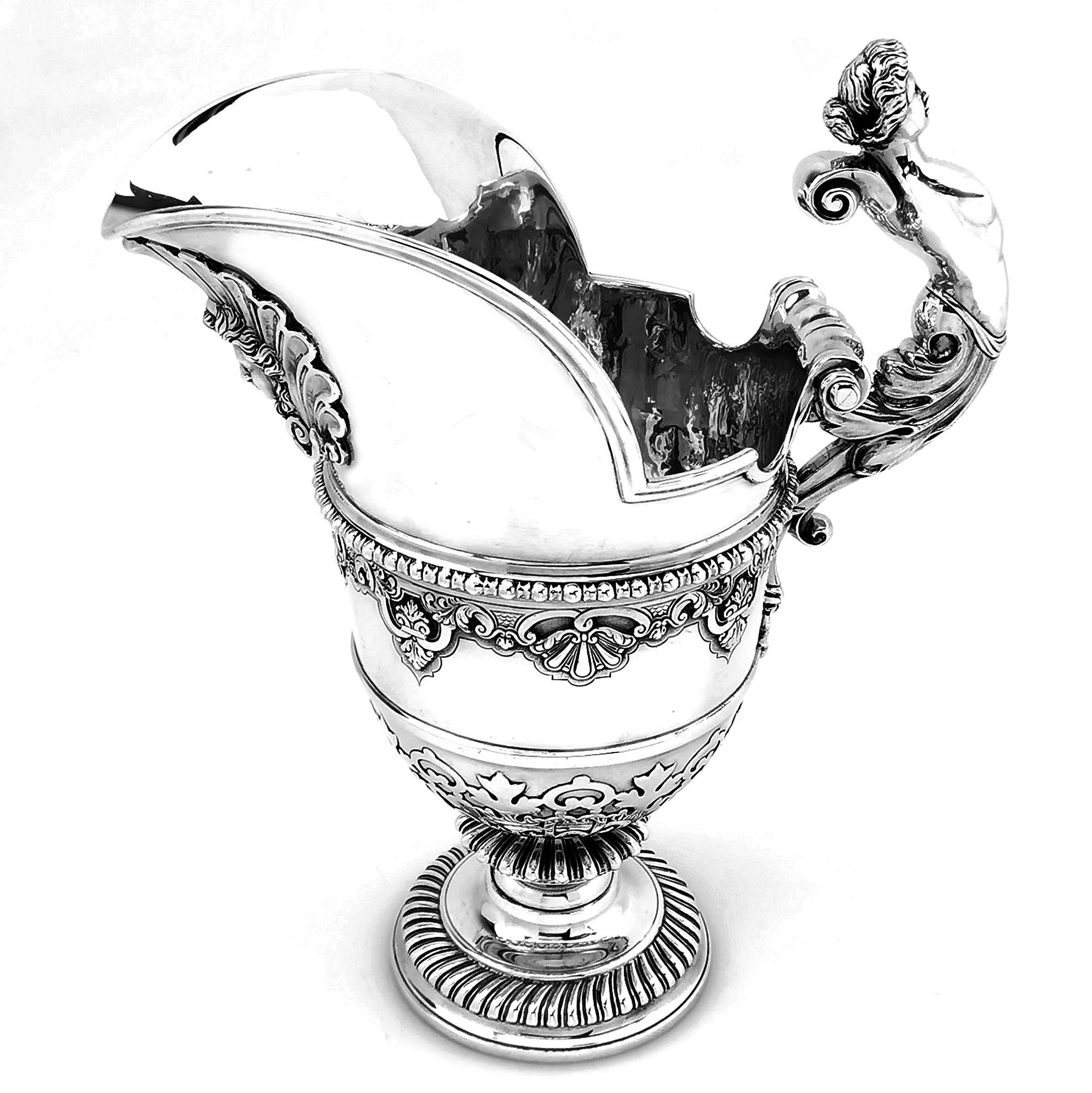 A magnificent Antique Solid Silver Jug with an impressive figural handle. The Jug has a broad spout and stands on a spread pedestal foot. The Jug has applied bands of decoration to the body and the spout has a shell with a face on the exterior.