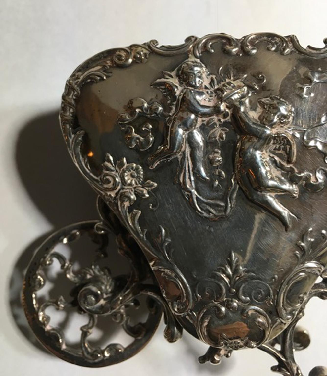 Antique baroque sterling silver little love cart  late 19th Century, Italy.

This a very nice and lovable piece of art fine art jewellery. Totally hand made. The surface is finely carved with floral decor and little angels.

Silver marks on the
