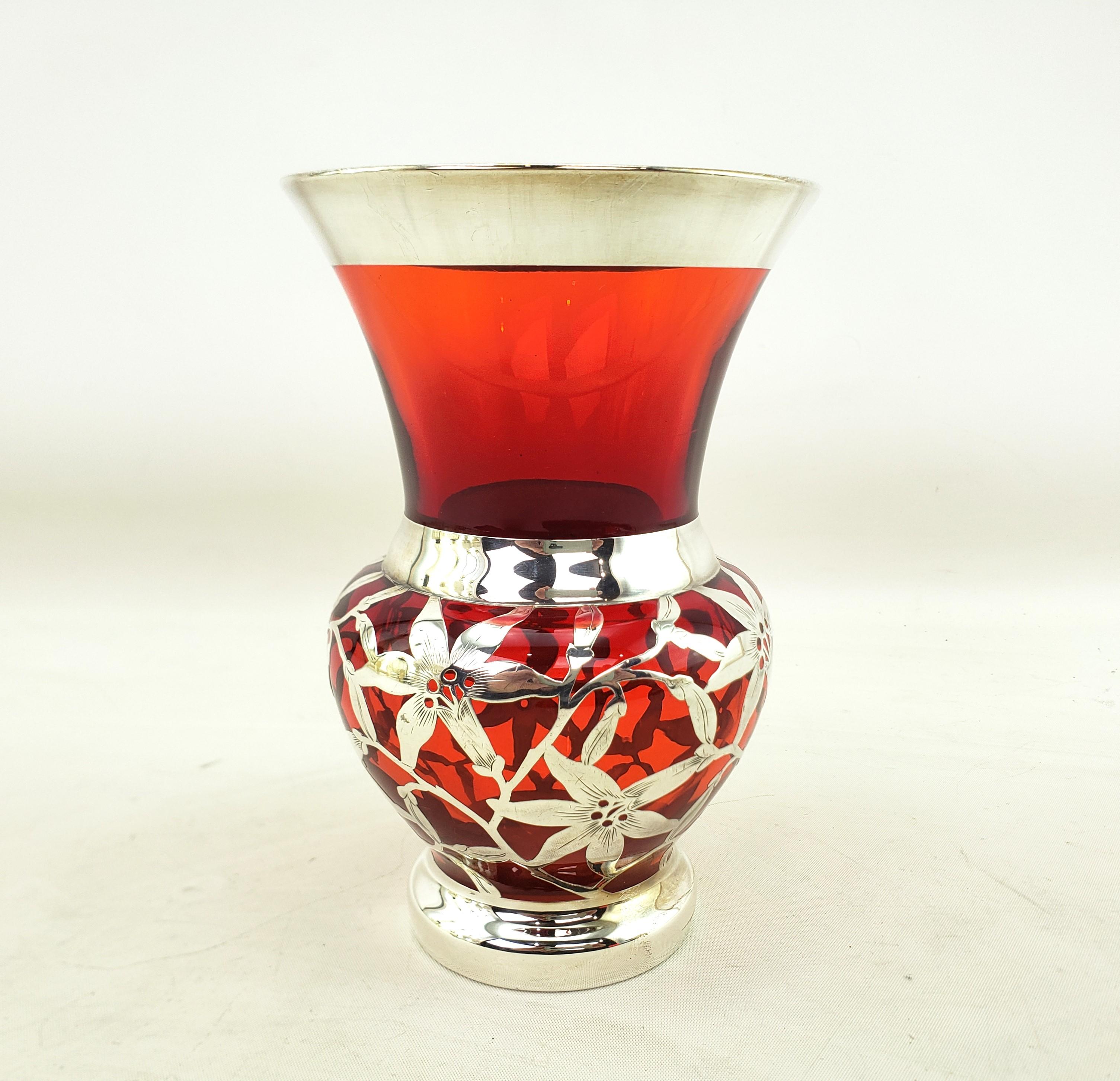 This well executed antique silver overlay vase is unsigned, but presumed to have originated from the United States and date to approximately 1920 and done in an Art Deco style. The vase is done with a thick ruby glass with heavy silver overlay