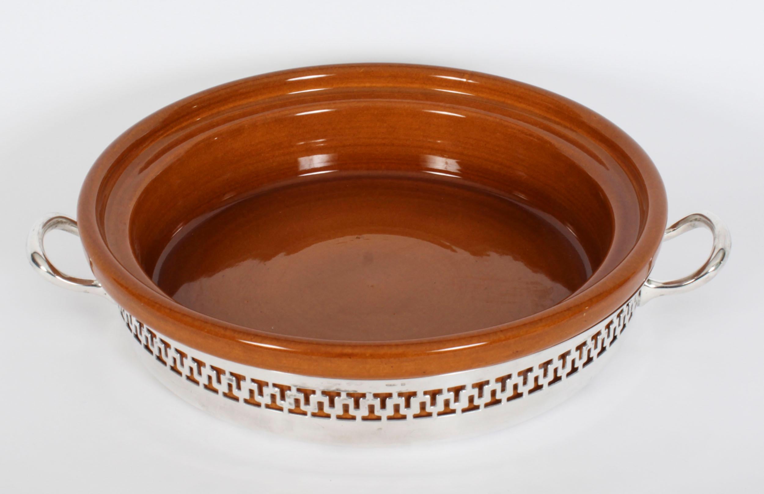 A decorative antique silver plate and terracotta casserole serving dish by Wiskemann, dating from the 1920s.
 
The round serving dish features a twin handled silver plated stand decorated with a pierced fretwork gallery.
 
Otto-Leonard Wiskemann