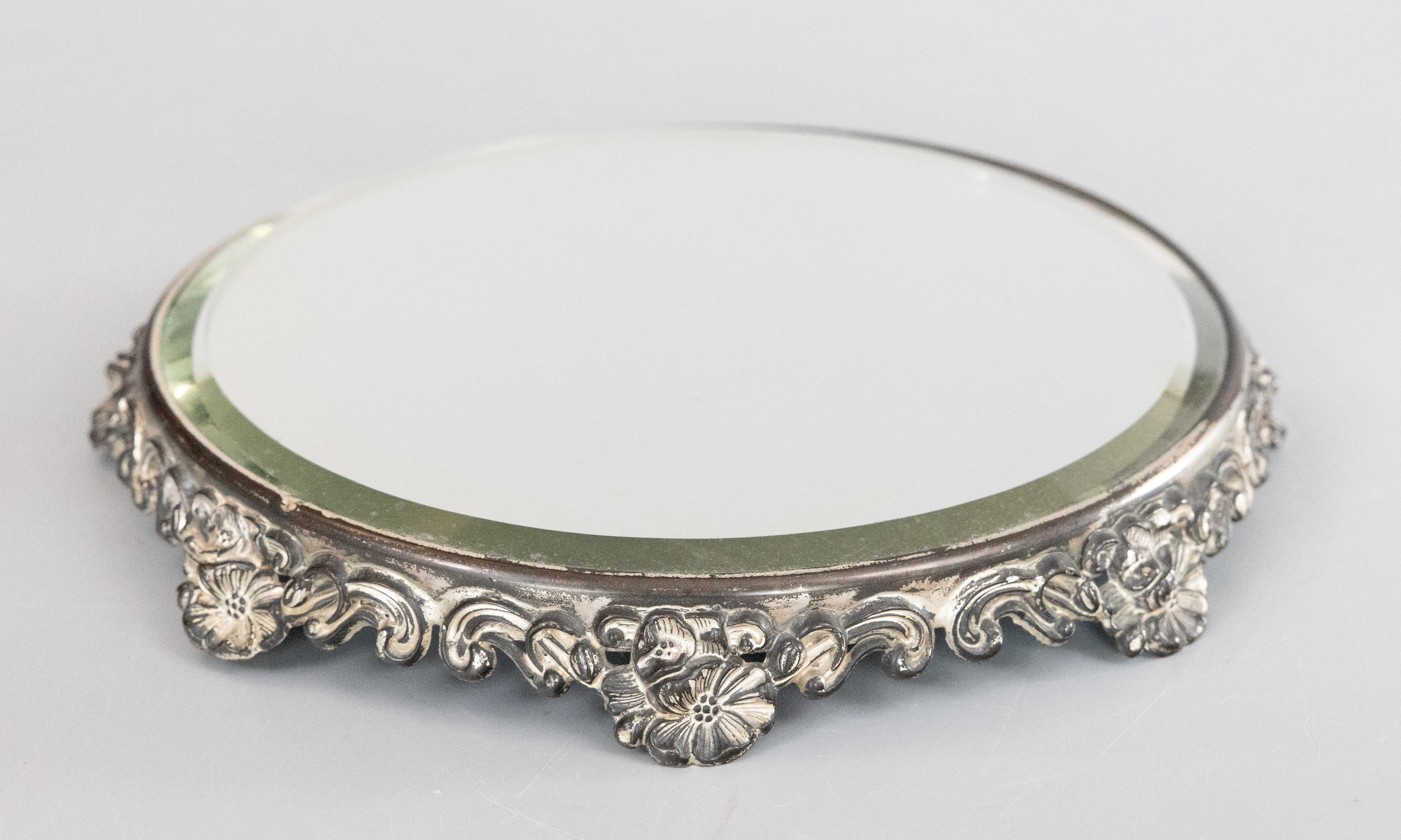 A lovely antique silverplate mirror plateau, circa 1920. No maker's mark. This beautiful plateau has an ornate floral design in a lovely silver patina and retains the original beveled mirror glass. It would look gorgeous displayed on a buffet with