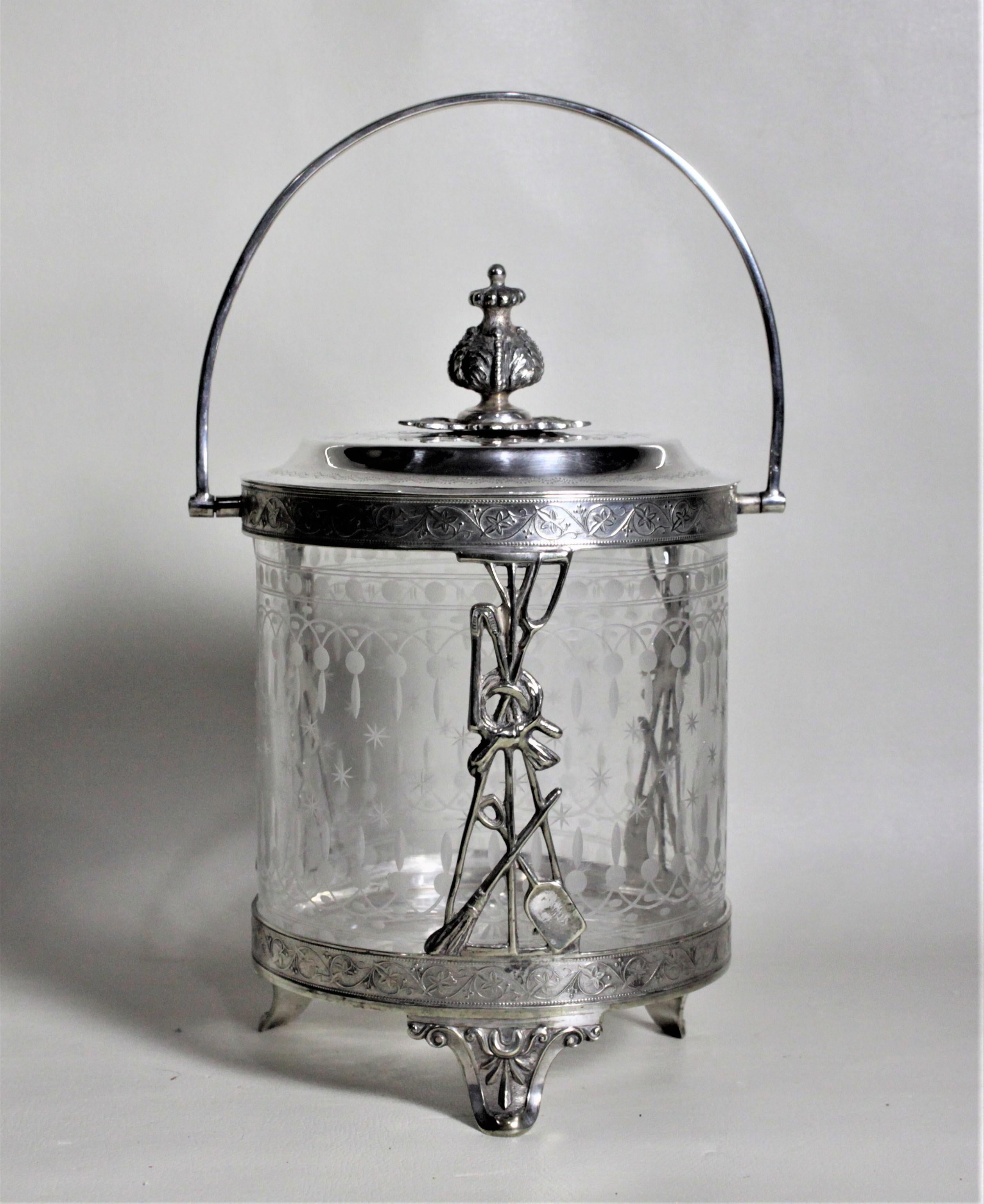 This unique biscuit barrel or cookie jar is unmarked, but believed to date to the Edwardian period and originate from England. The frame of this biscuit barrel is ornately engraved with a scroll and floral motif around both the upper and lower bands