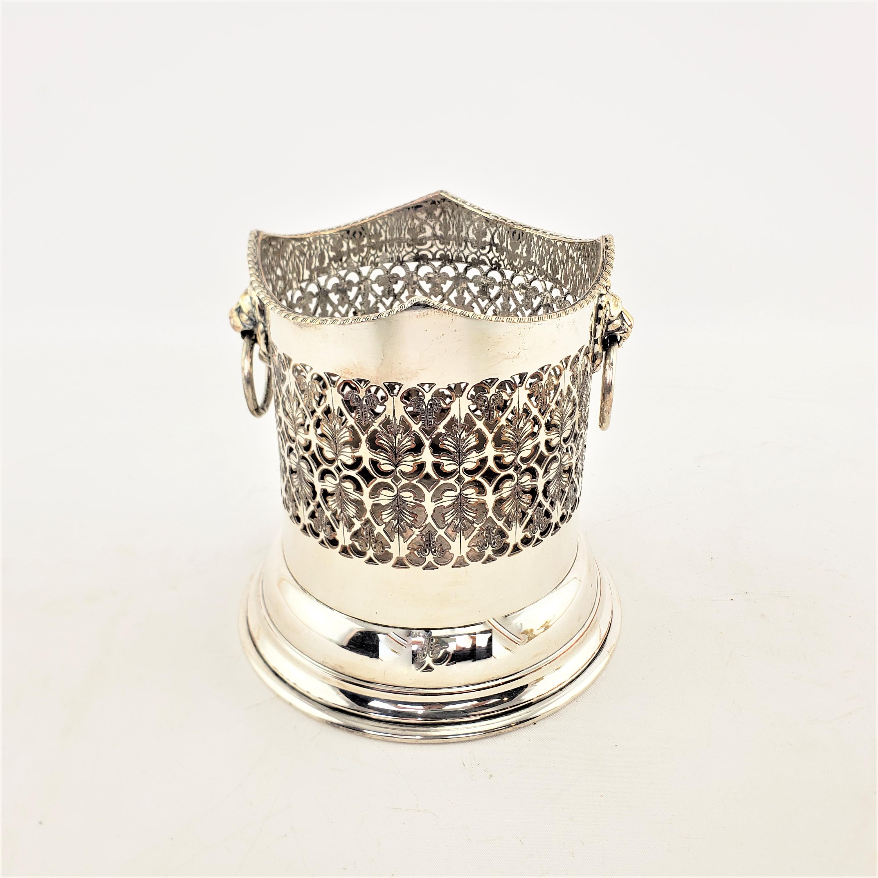 This antique bottle coaster is unsigned, but presumed to have originate from England and date to approximately 1920 and done in a Victorian style. This bottle coaster is composed of silver plate over copper with figural lion head mounted handles,