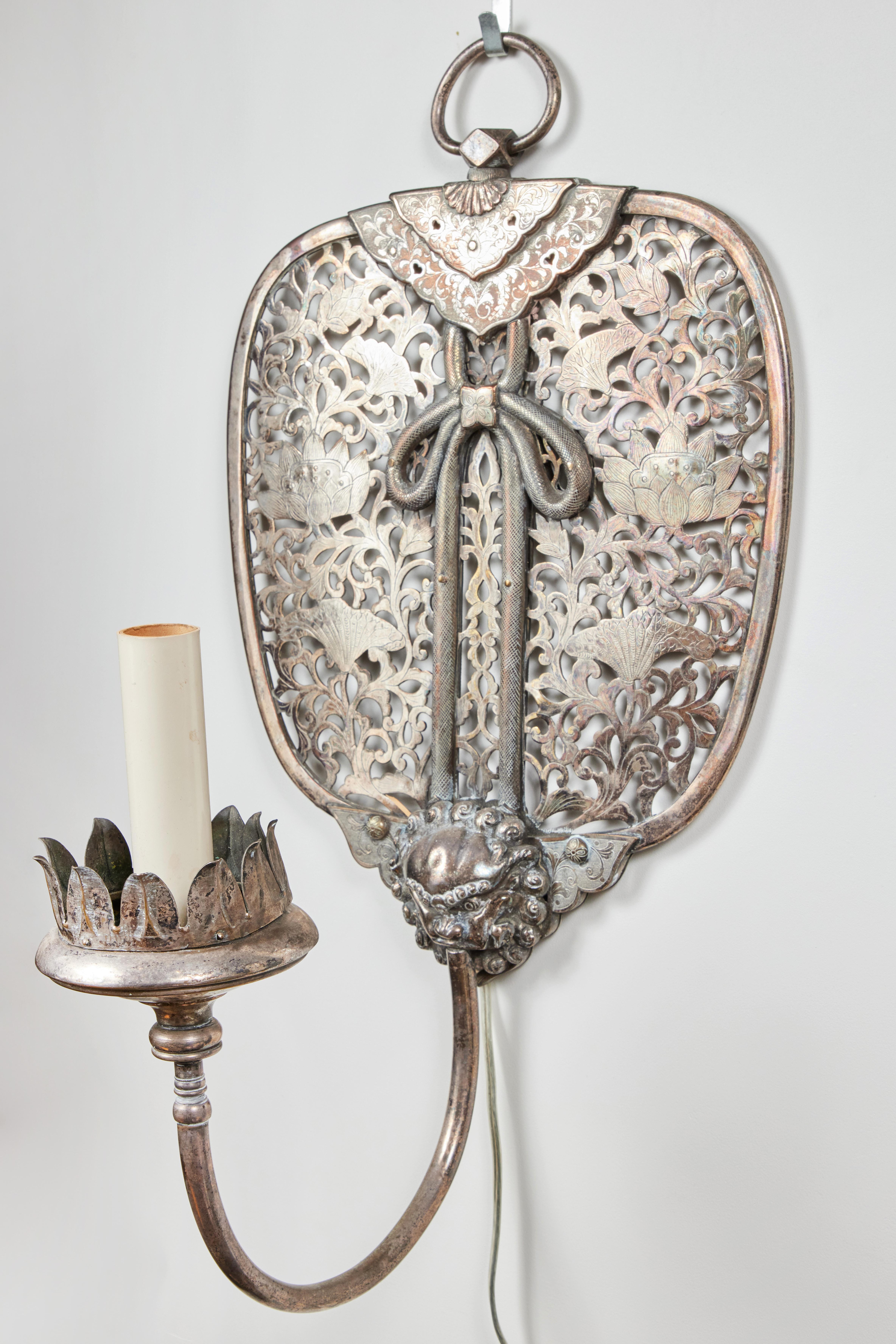 A pair of remarkable, silvered, French wall sconces in the Chinoiserie style. Each with large, pierced screens filled with blossoming lotus flowers surrounded by foliate scrolls and centered with a dripping bow that descends to a foo dog grasping a